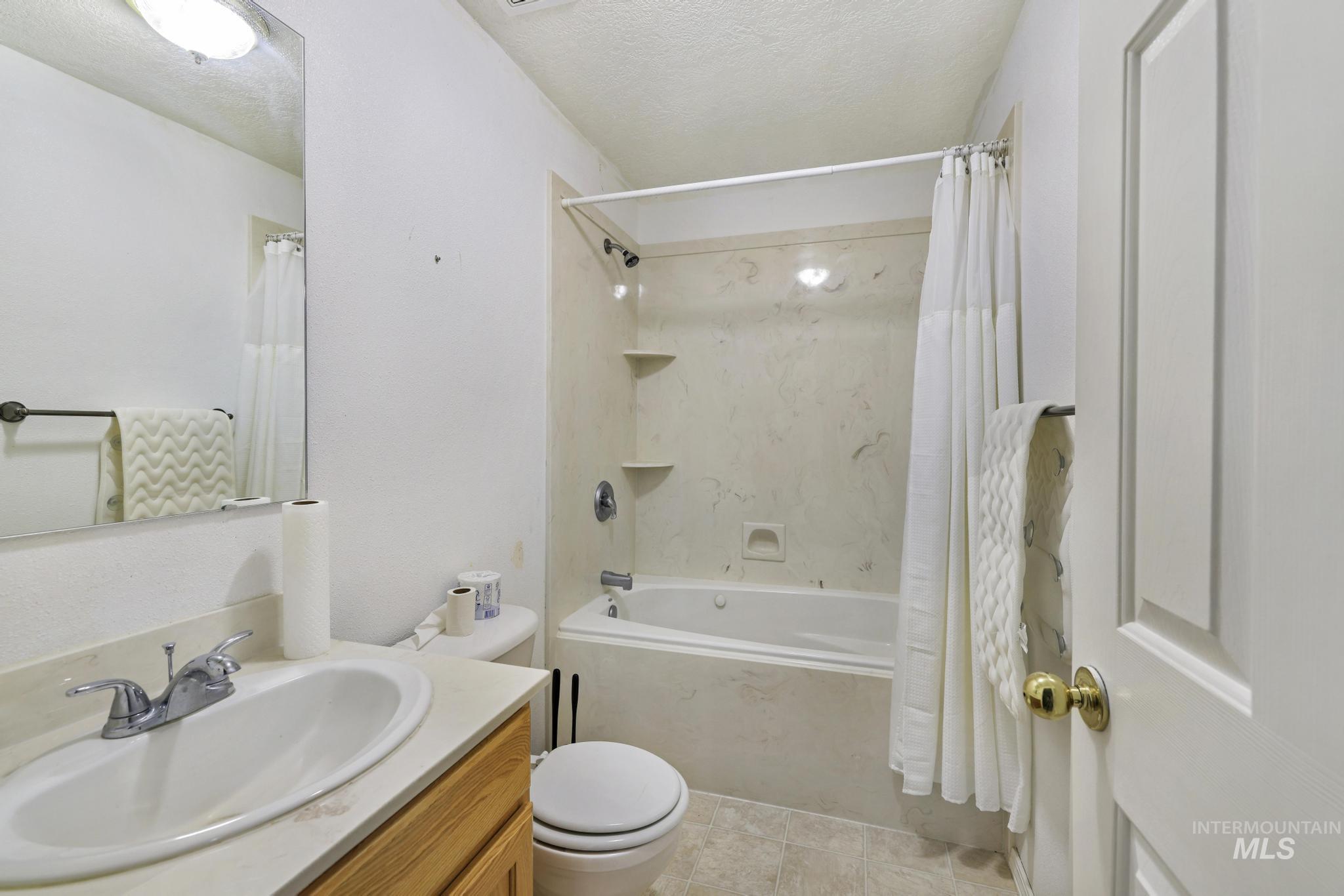 Bathroom with vanity, a textured ceiling, shower / bathtub combination with curtain, and light tile patterned floors