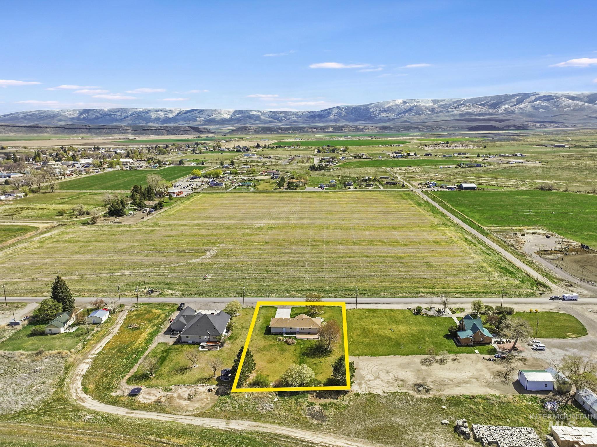 Aerial view of sparsely populated area featuring property parcel outlined, a mountain backdrop, and rows of crops