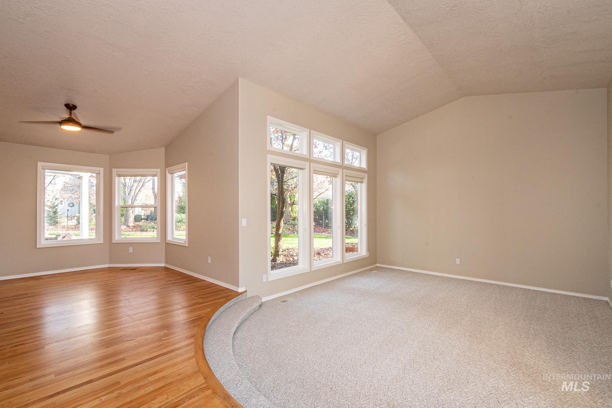 Empty room featuring a textured ceiling, vaulted ceiling, light wood finished floors, and ceiling fan