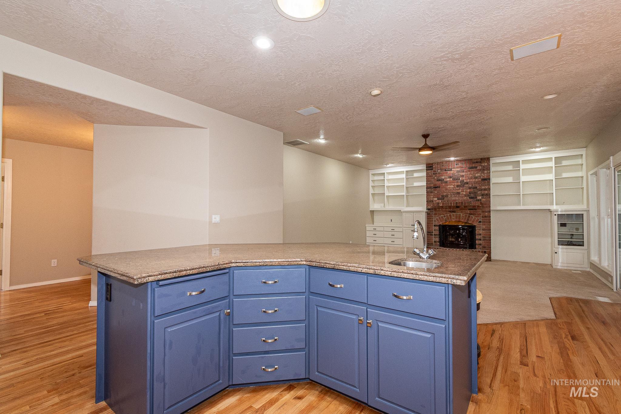 Kitchen with open floor plan, a textured ceiling, a fireplace, blue cabinets, and light wood finished floors