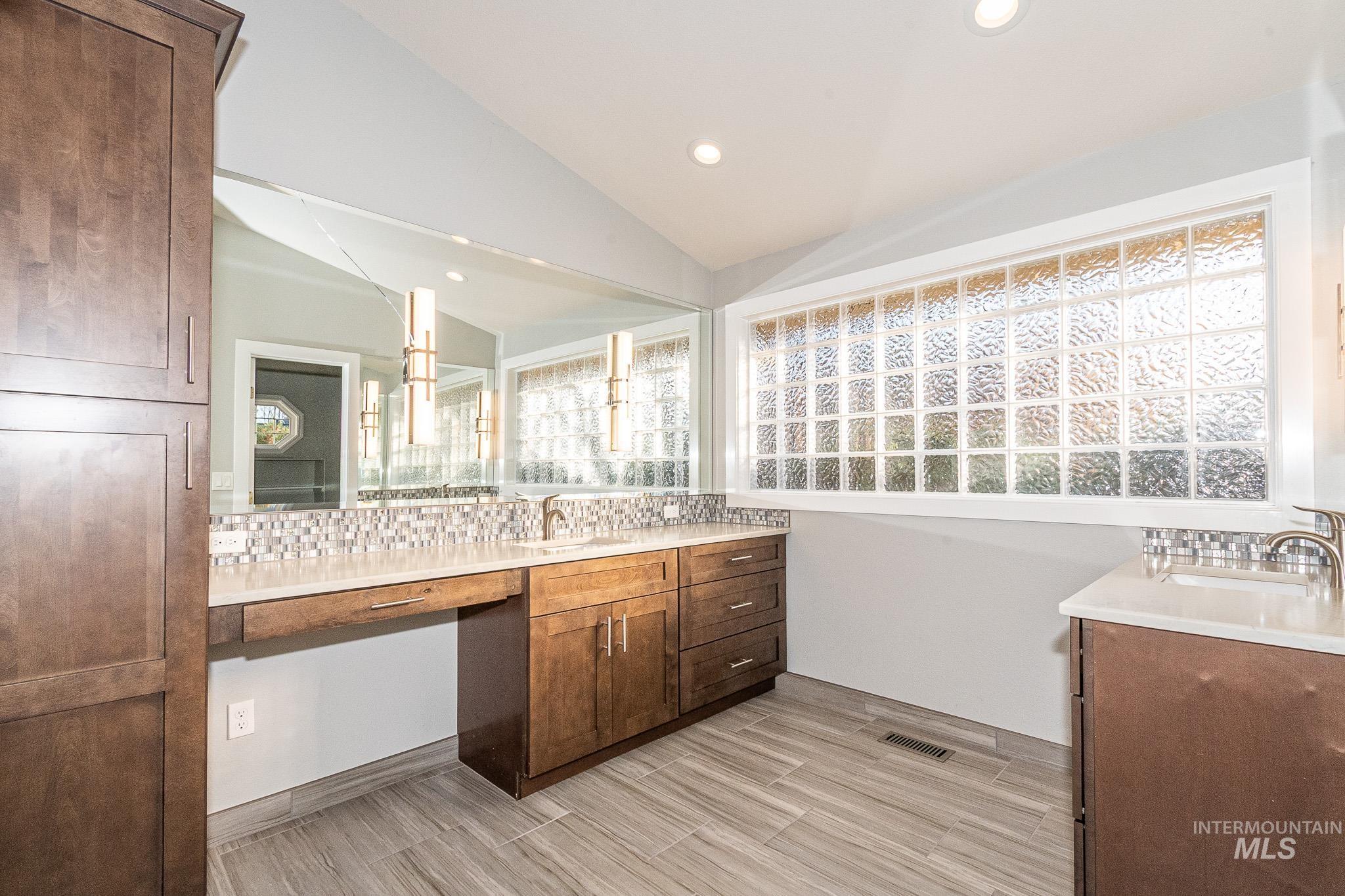 Full bathroom featuring two vanities, recessed lighting, lofted ceiling, decorative backsplash, and light wood-style floors