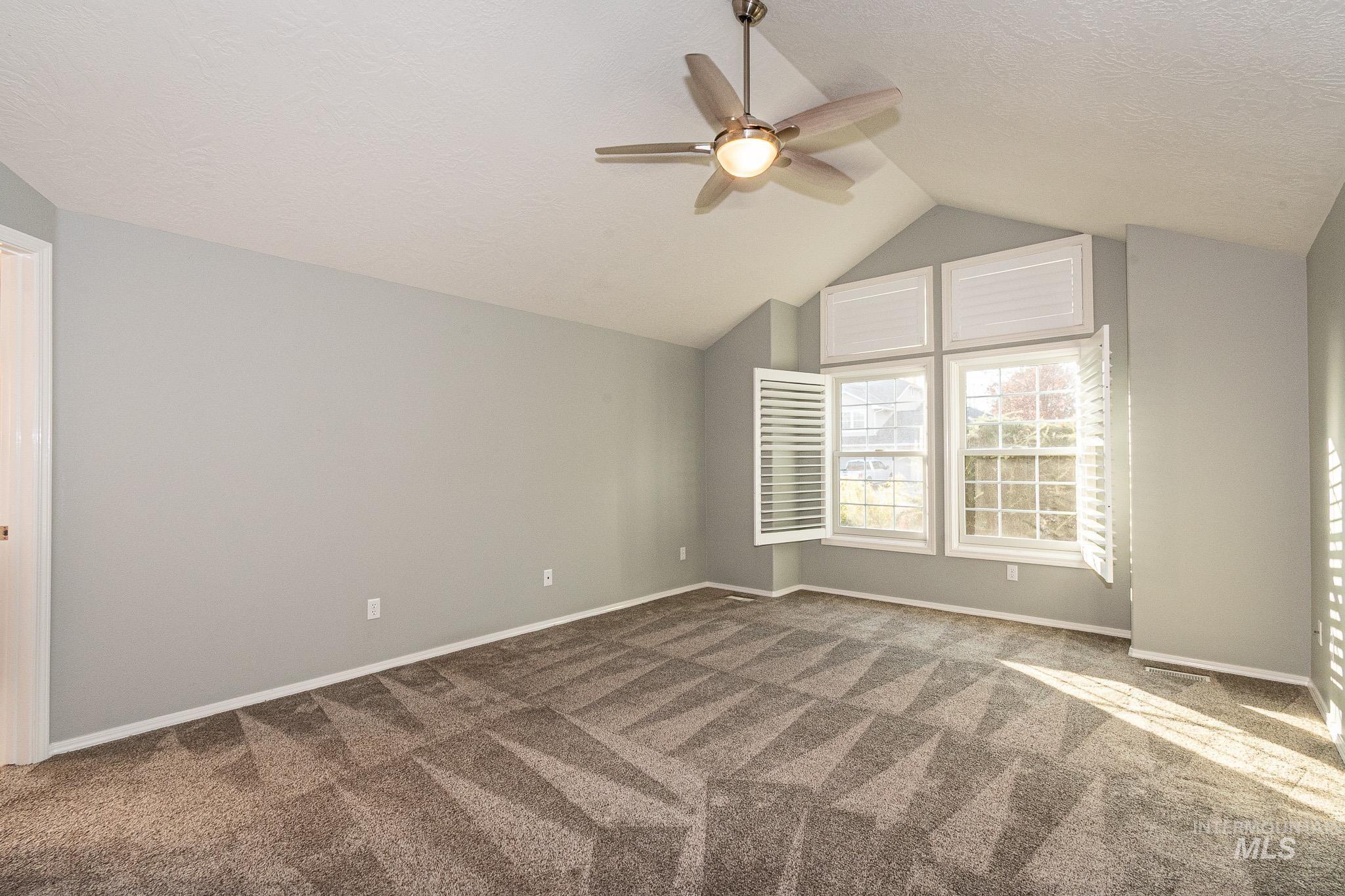 Carpeted empty room with a textured ceiling, a ceiling fan, and vaulted ceiling