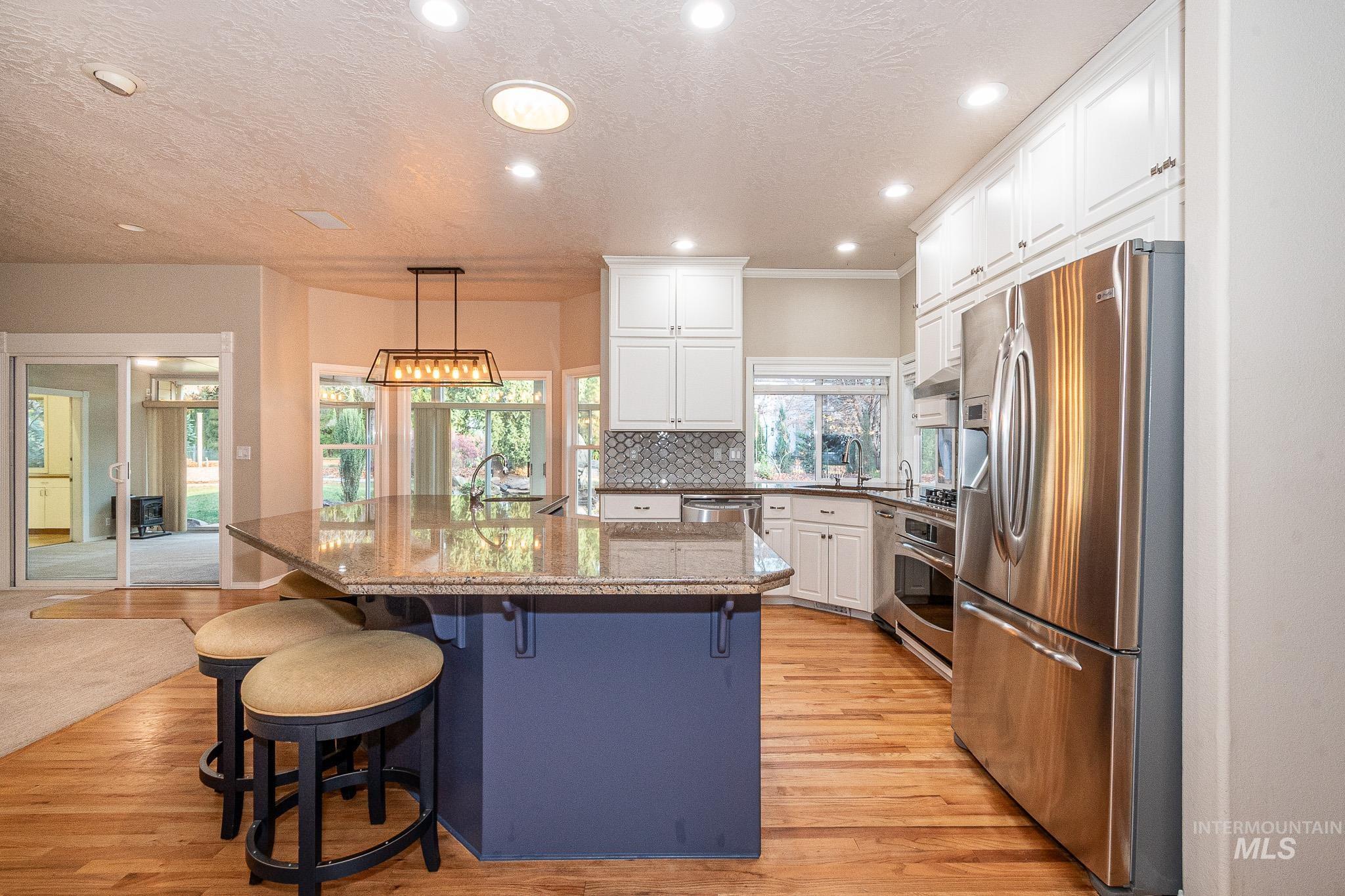 Kitchen with stainless steel appliances, dark stone countertops, white cabinets, a textured ceiling, and a kitchen breakfast bar