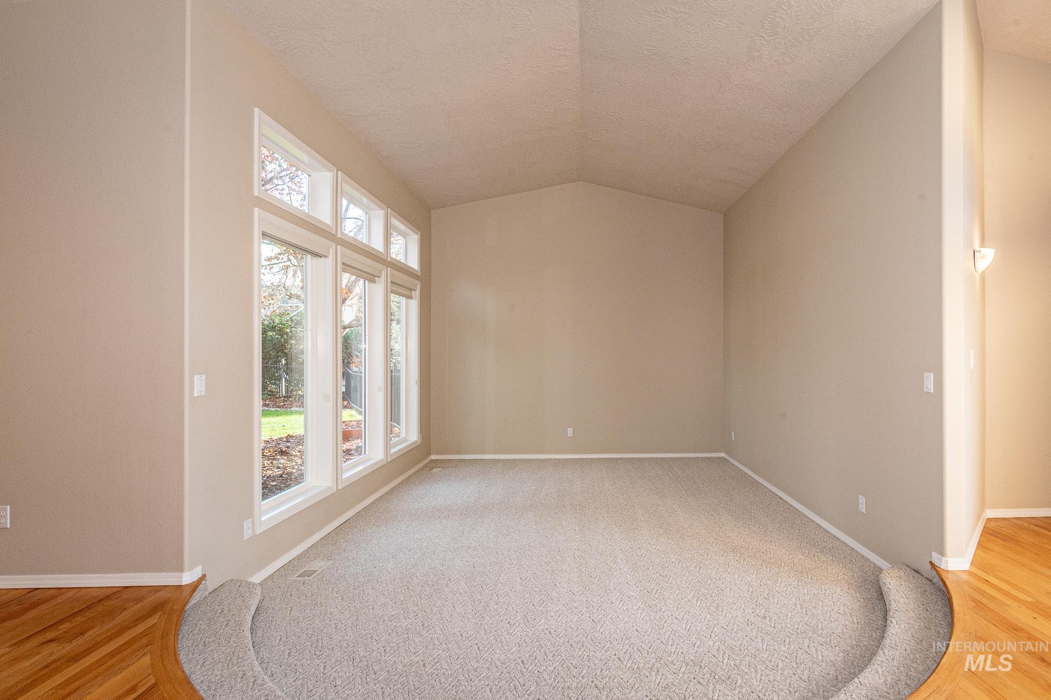 Spare room with lofted ceiling, light wood-style flooring, and a textured ceiling