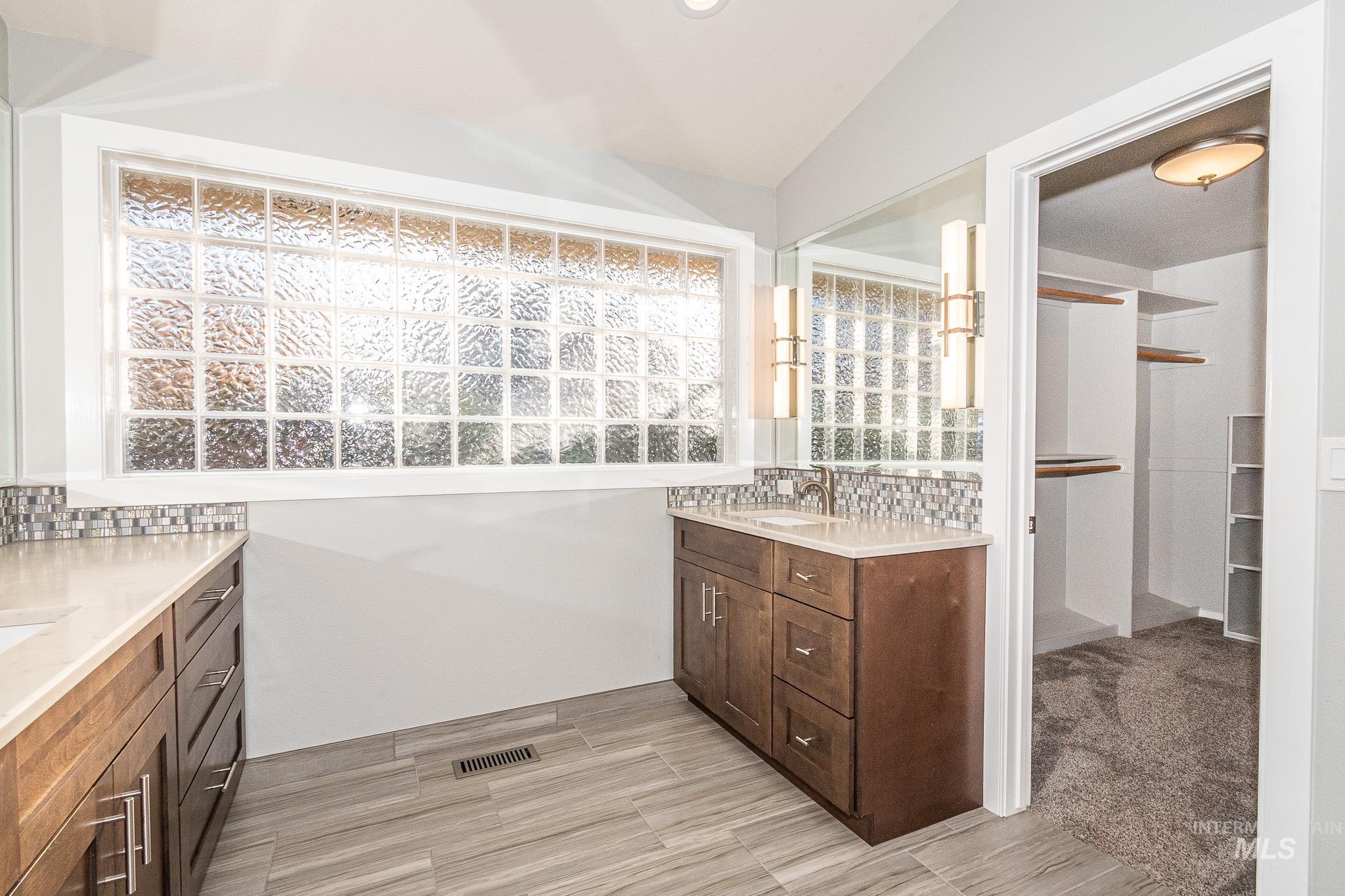 Full bathroom featuring vanity, tasteful backsplash, light wood-style flooring, and a spacious closet
