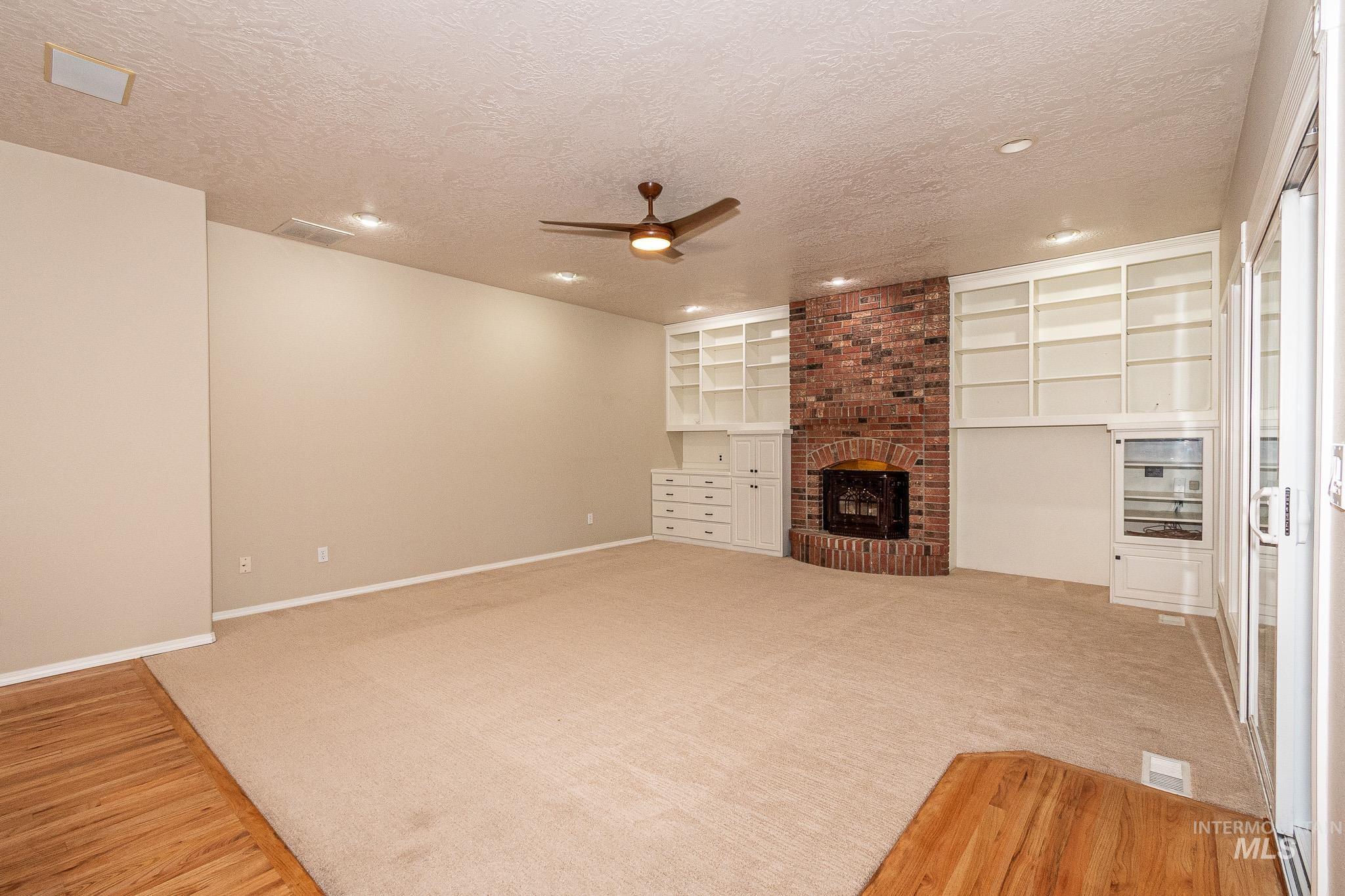 Unfurnished living room featuring a fireplace, ceiling fan, a textured ceiling, built in features, and light colored carpet