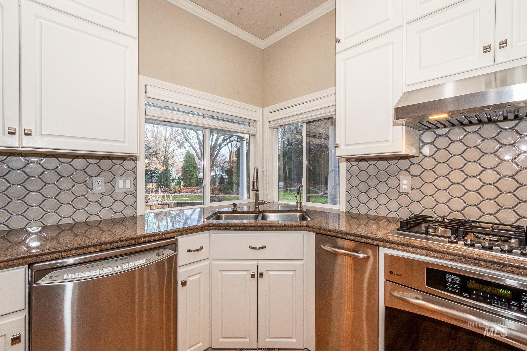 Kitchen featuring stainless steel appliances, crown molding, tasteful backsplash, white cabinetry, and dark stone countertops