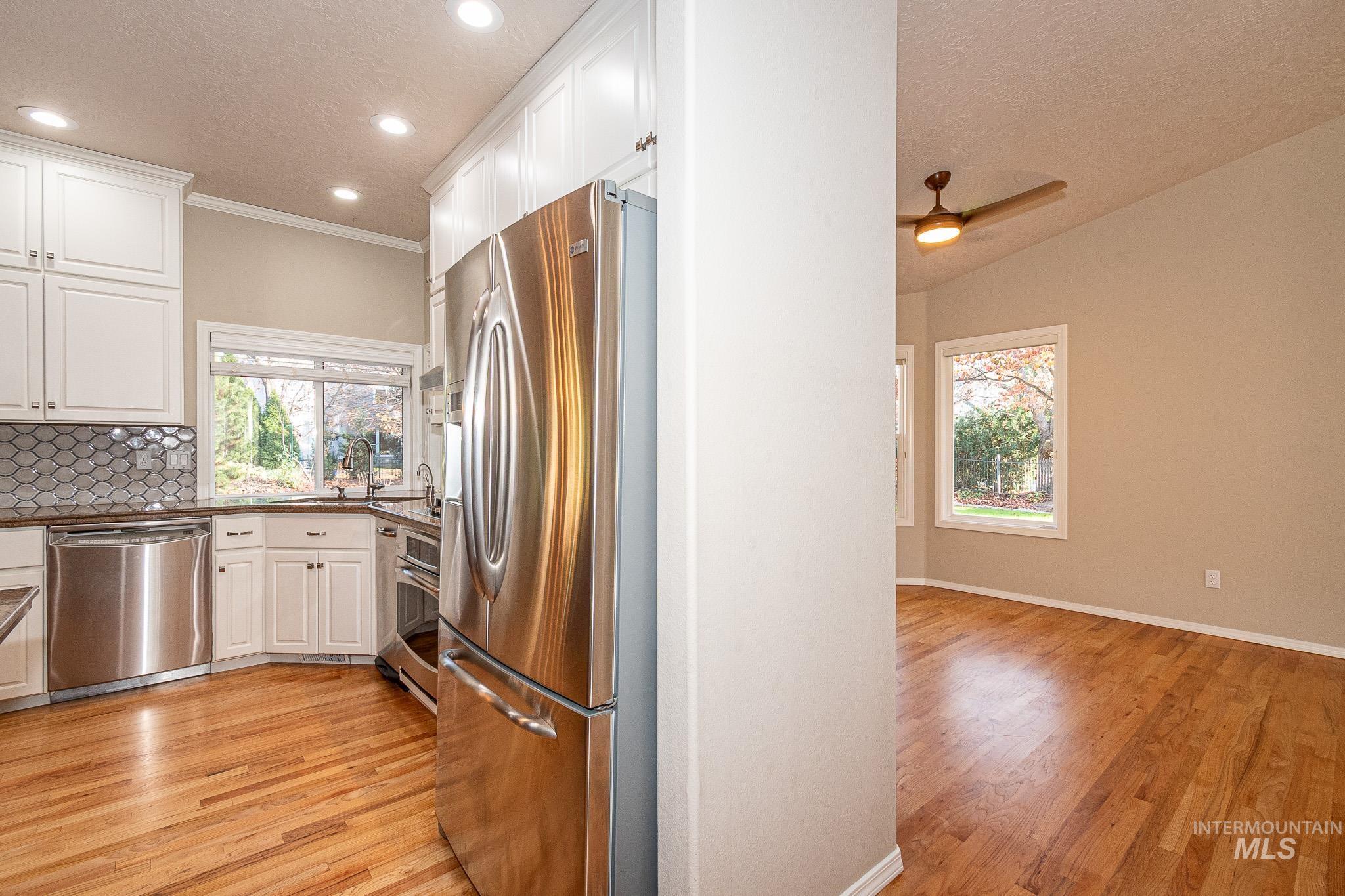 Kitchen with light wood finished floors, appliances with stainless steel finishes, a textured ceiling, backsplash, and white cabinets
