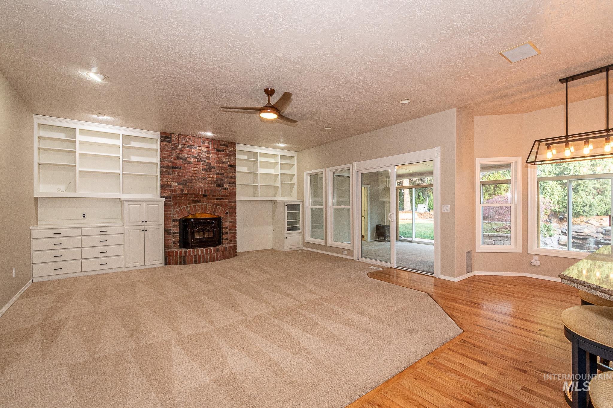 Unfurnished living room featuring a textured ceiling, built in shelves, a ceiling fan, light wood finished floors, and a brick fireplace