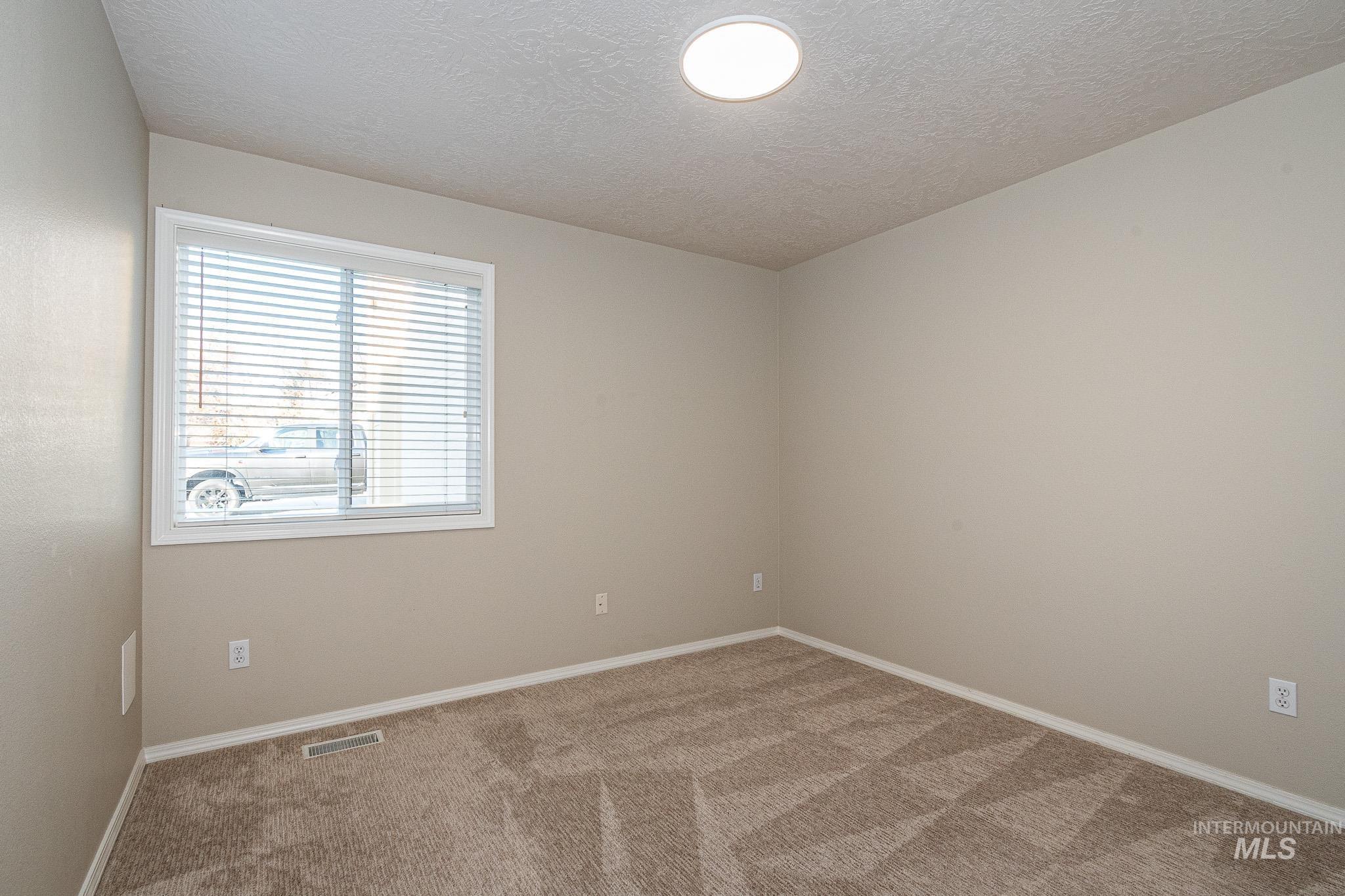 Carpeted empty room with a textured ceiling and baseboards
