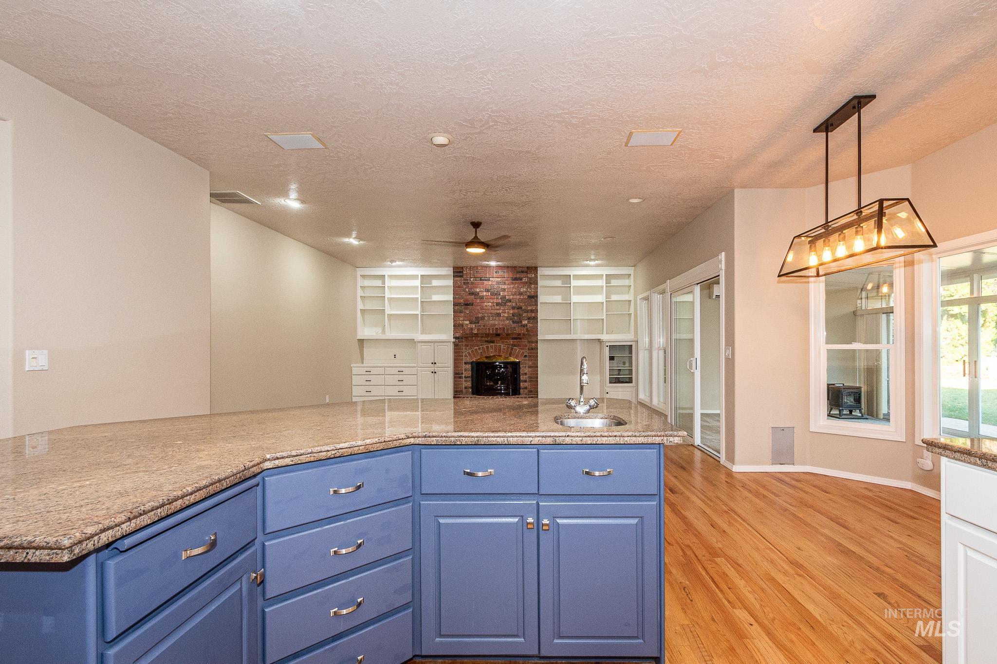 Kitchen with blue cabinetry, a brick fireplace, light wood-style flooring, a textured ceiling, and open floor plan