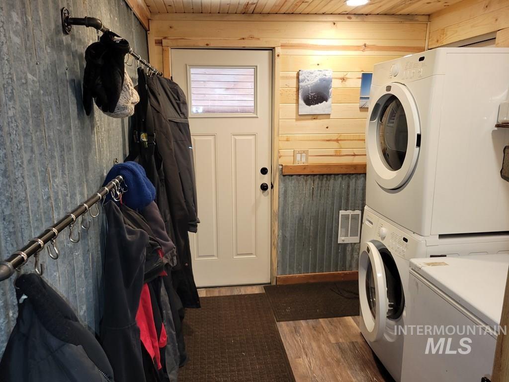 Washroom with dark wood-type flooring, wood walls, stacked washing machine and dryer, and heating unit