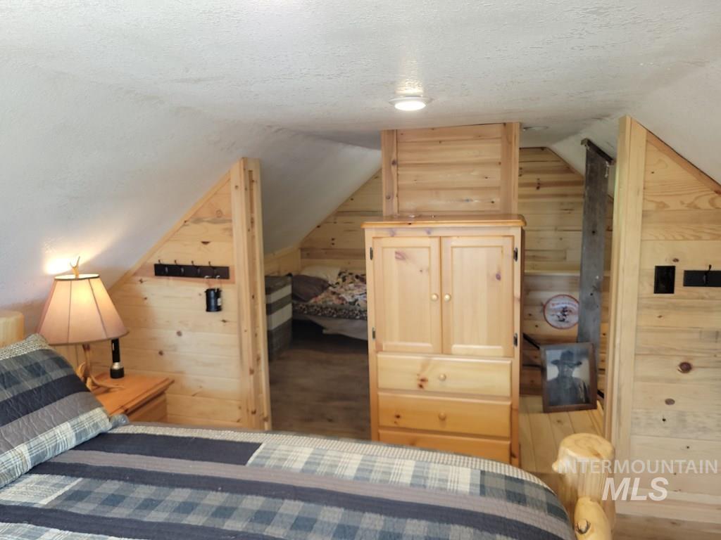 Bedroom featuring wood walls, a textured ceiling, vaulted ceiling, and wood finished floors