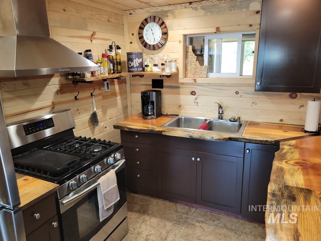 Kitchen featuring stainless steel appliances, wall chimney range hood, butcher block countertops, wooden walls, and open shelves
