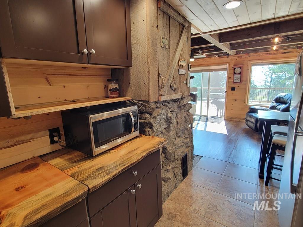 Kitchen with wood walls, dark brown cabinets, stainless steel appliances, butcher block counters, and beamed ceiling