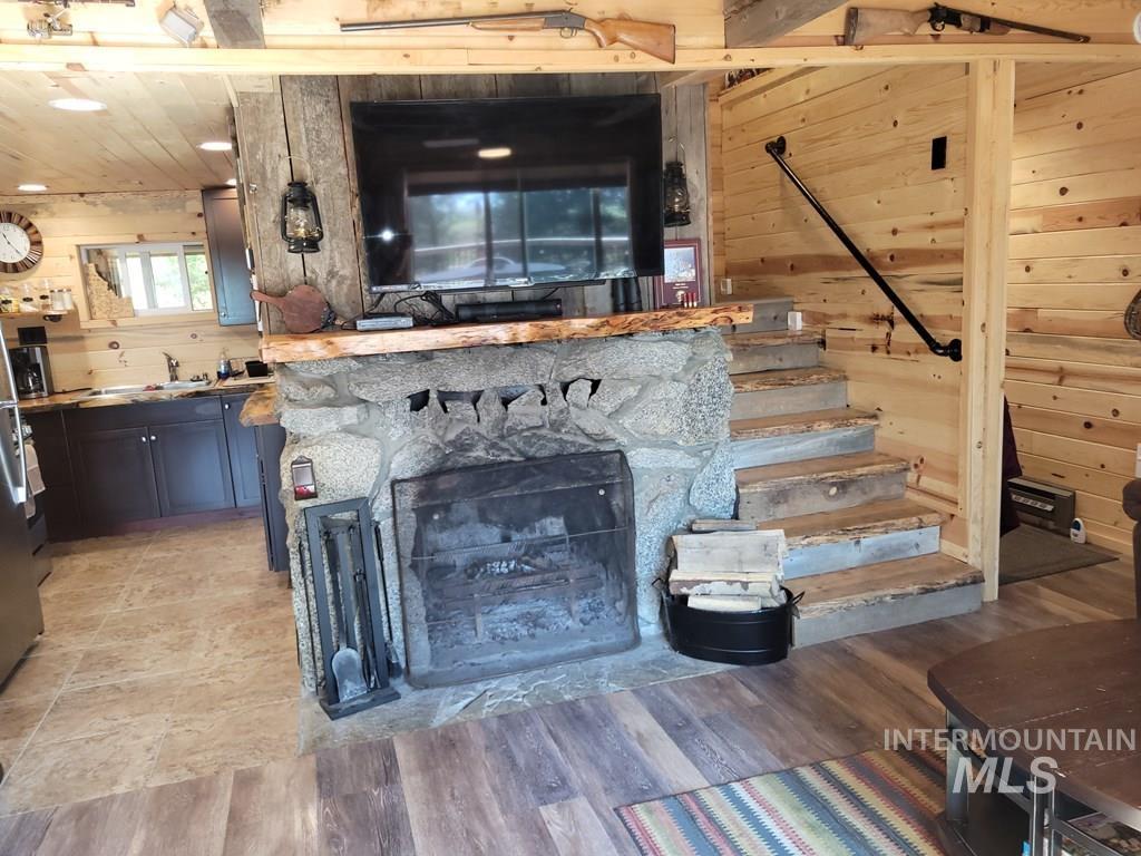 Living room with wood walls, stairs, a stone fireplace, and light wood-type flooring