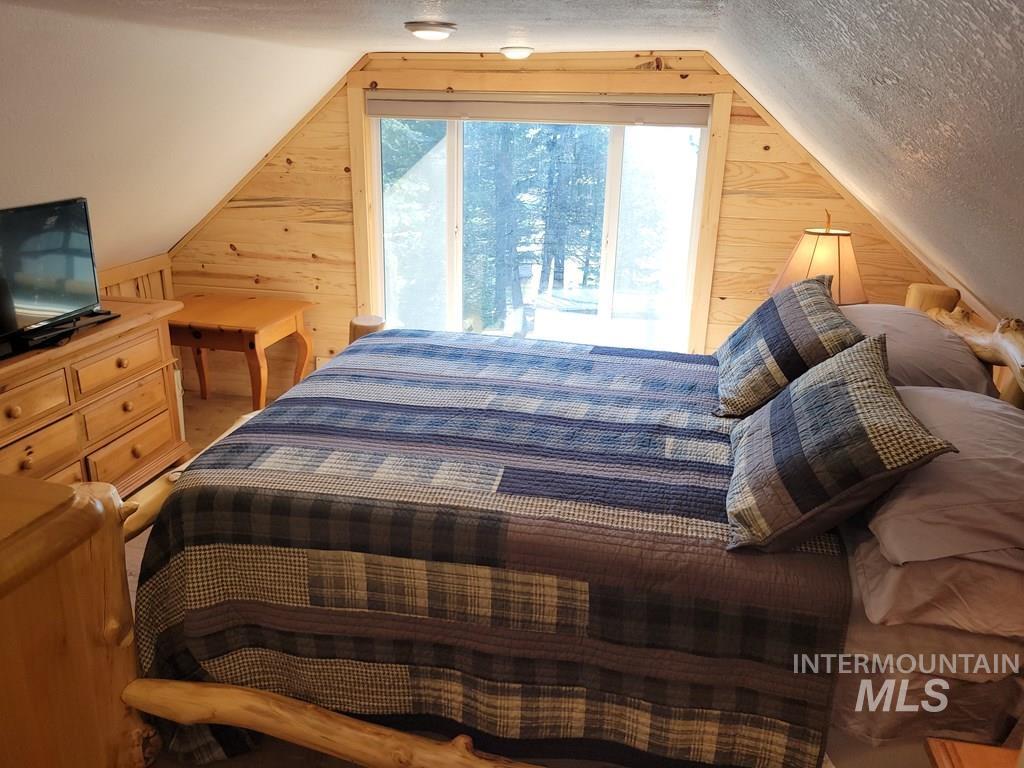 Bedroom with wood walls, access to exterior, a textured ceiling, and lofted ceiling