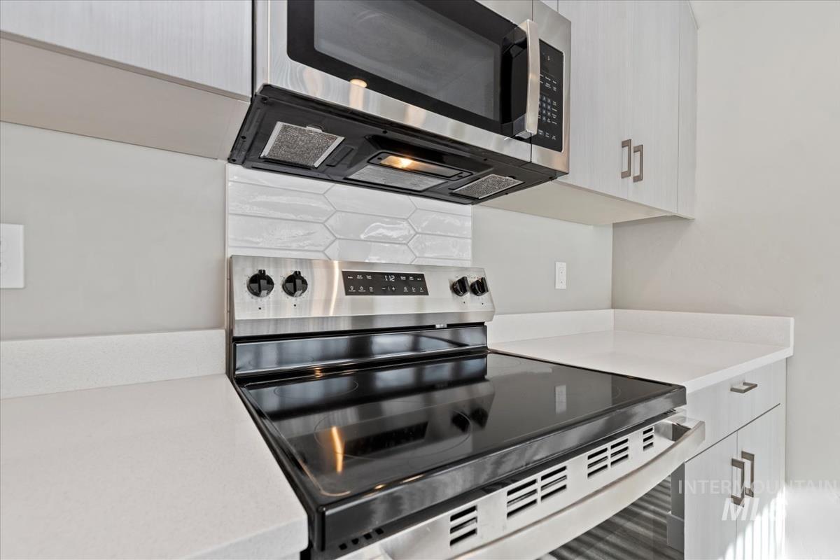 Kitchen featuring stainless steel appliances, white cabinets, backsplash, and light stone counters