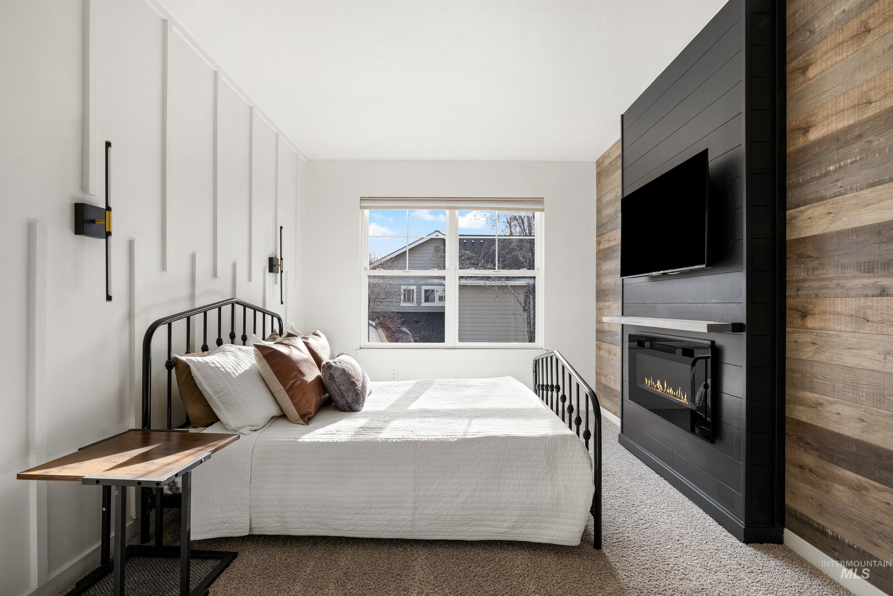 Carpeted bedroom with a large fireplace and wood walls