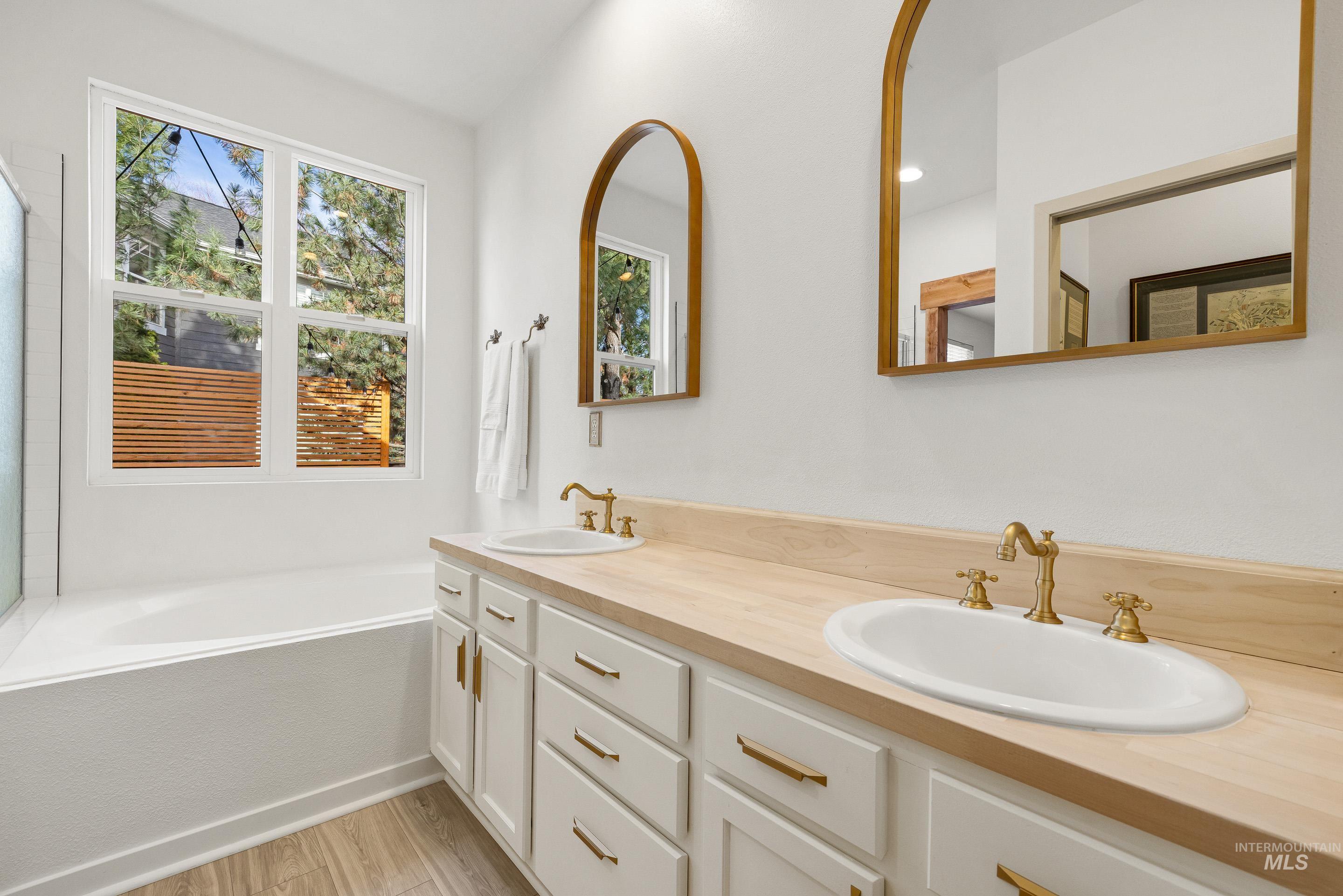 Bathroom with double vanity, a bath, healthy amount of natural light, and light wood-type flooring
