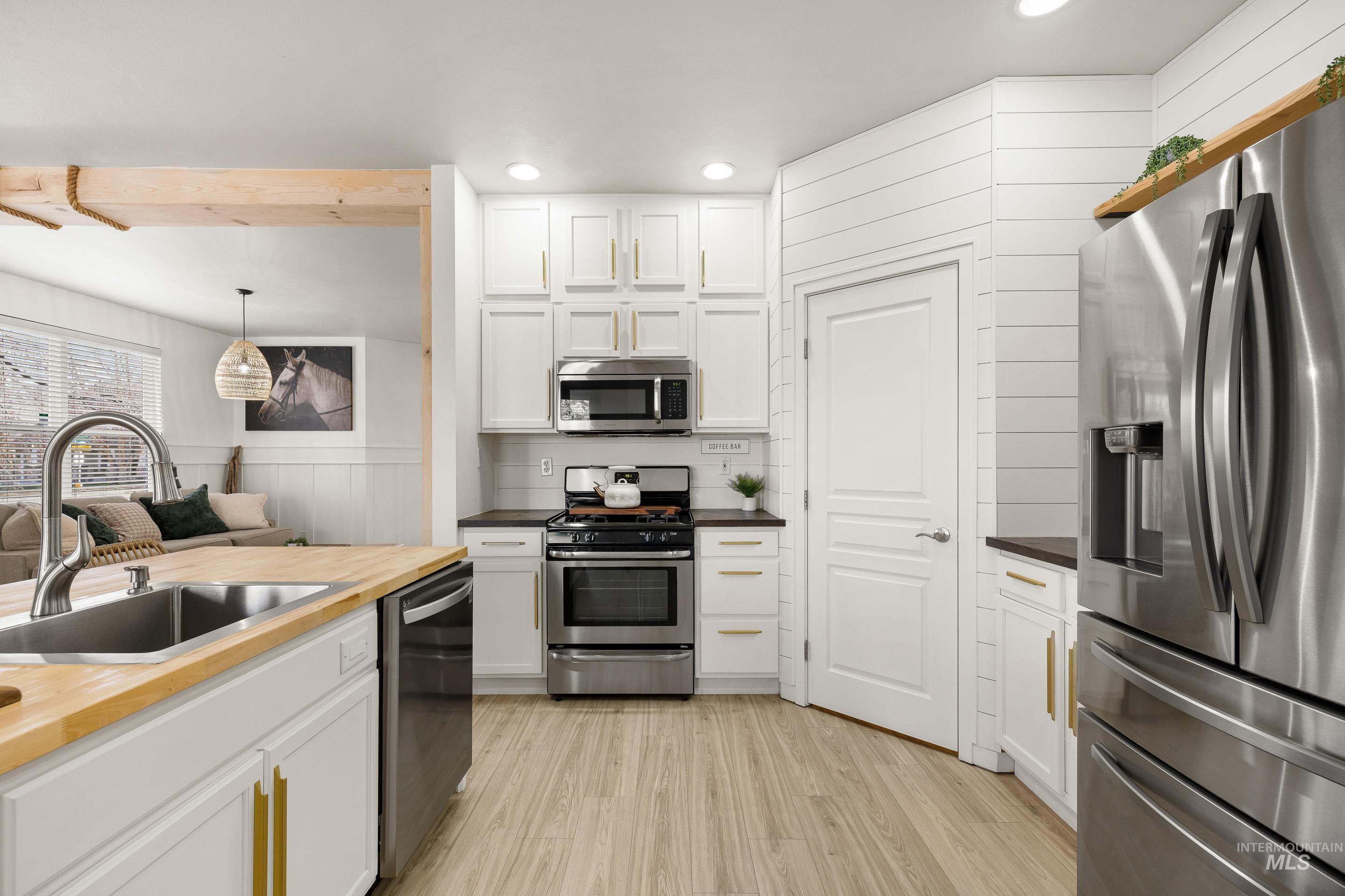 Kitchen featuring butcher block countertops, stainless steel appliances, white cabinetry, decorative light fixtures, and light wood-type flooring