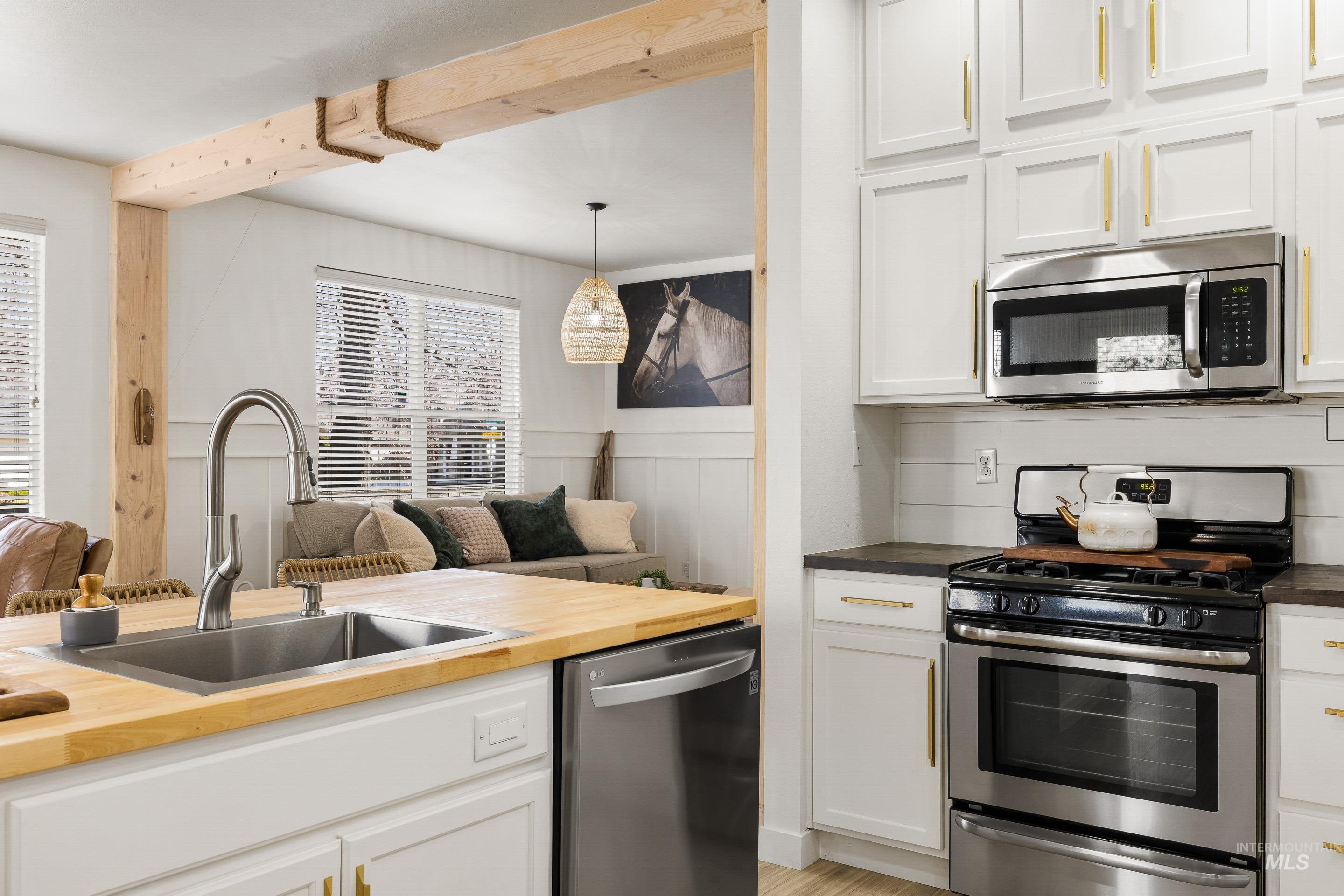 Kitchen featuring wooden counters, stainless steel appliances, white cabinetry, and pendant lighting