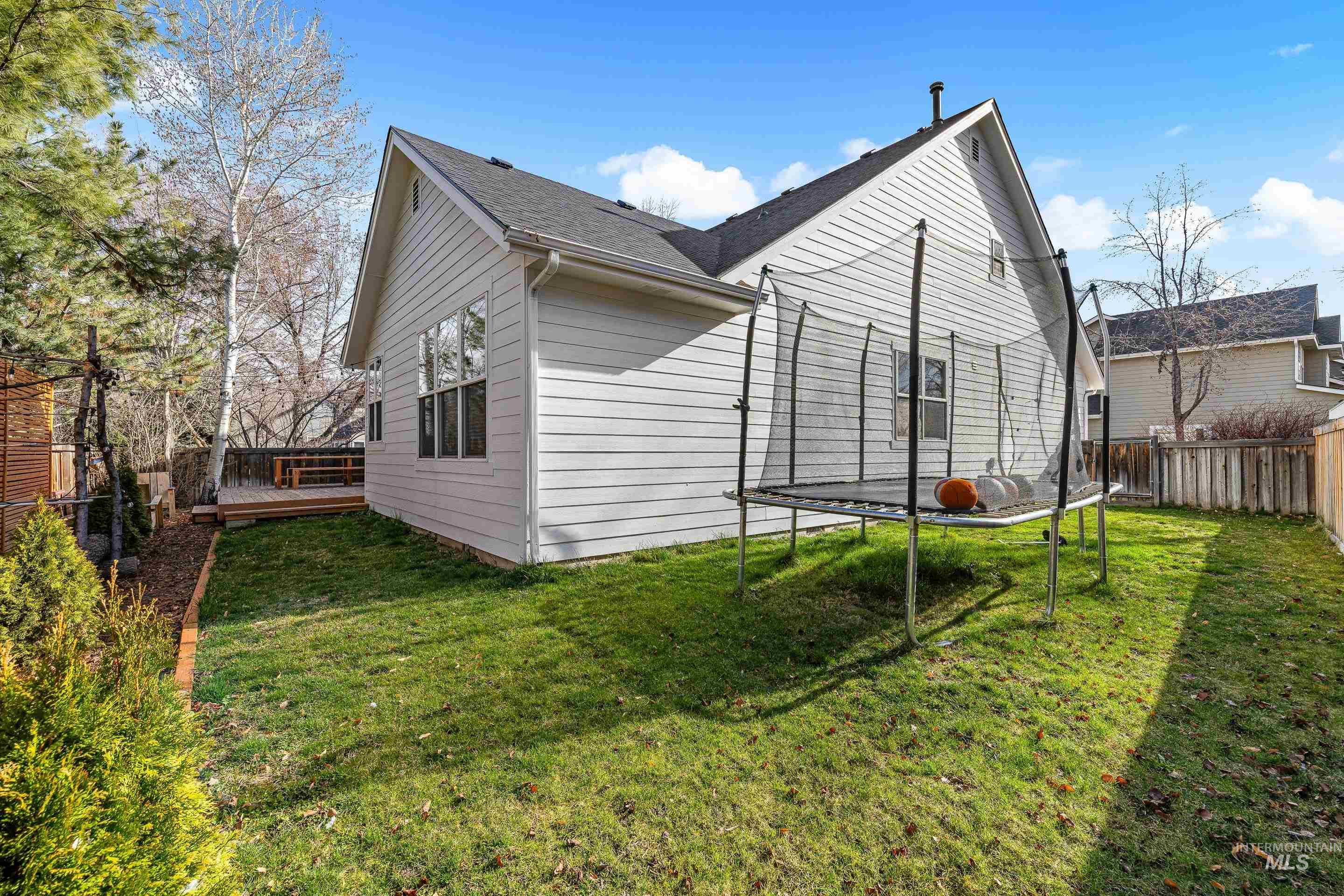 View of side of home with a trampoline, a deck, a fenced backyard, and a shingled roof