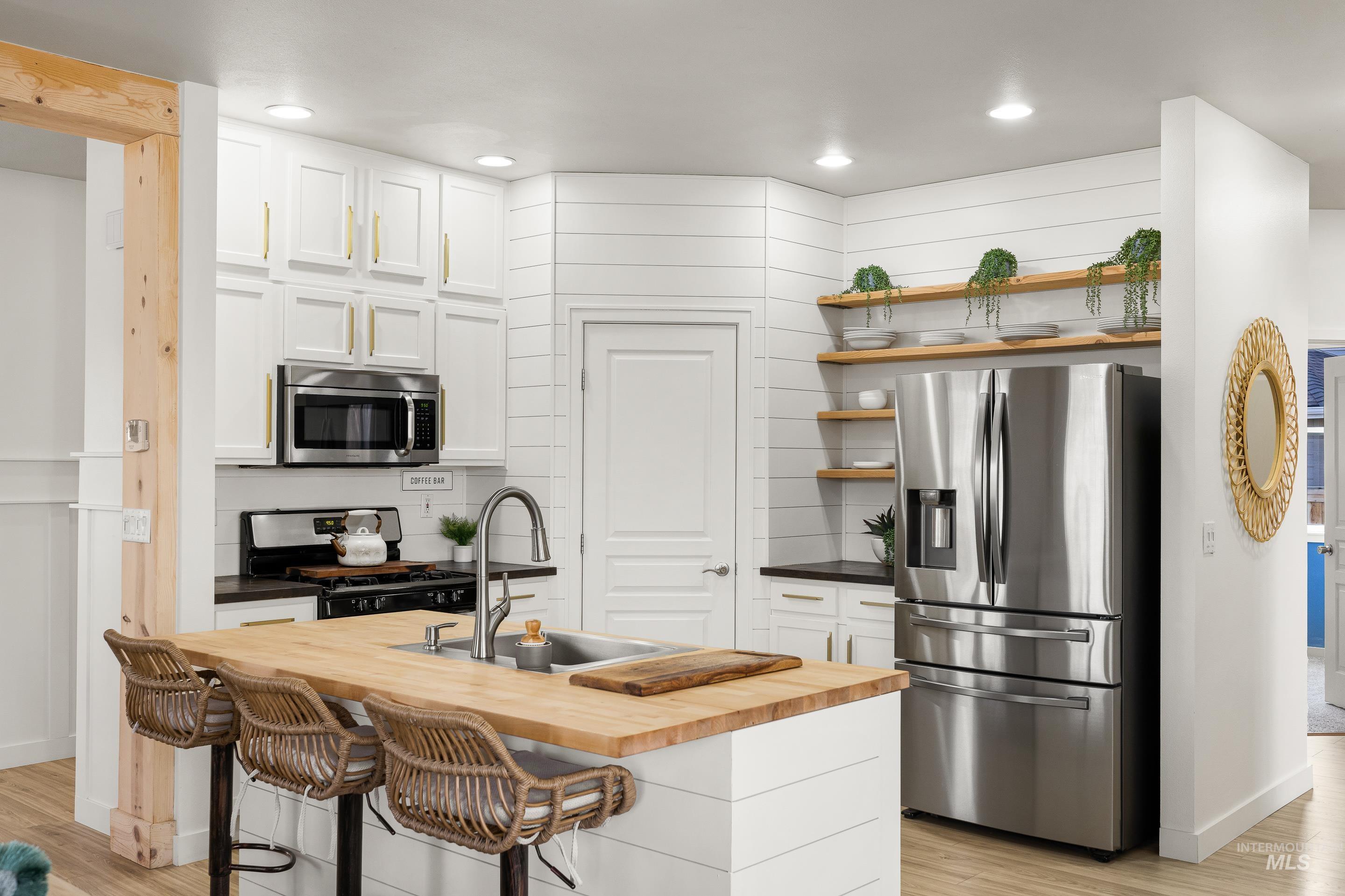 Kitchen with wooden counters, stainless steel appliances, white cabinetry, open shelves, and recessed lighting