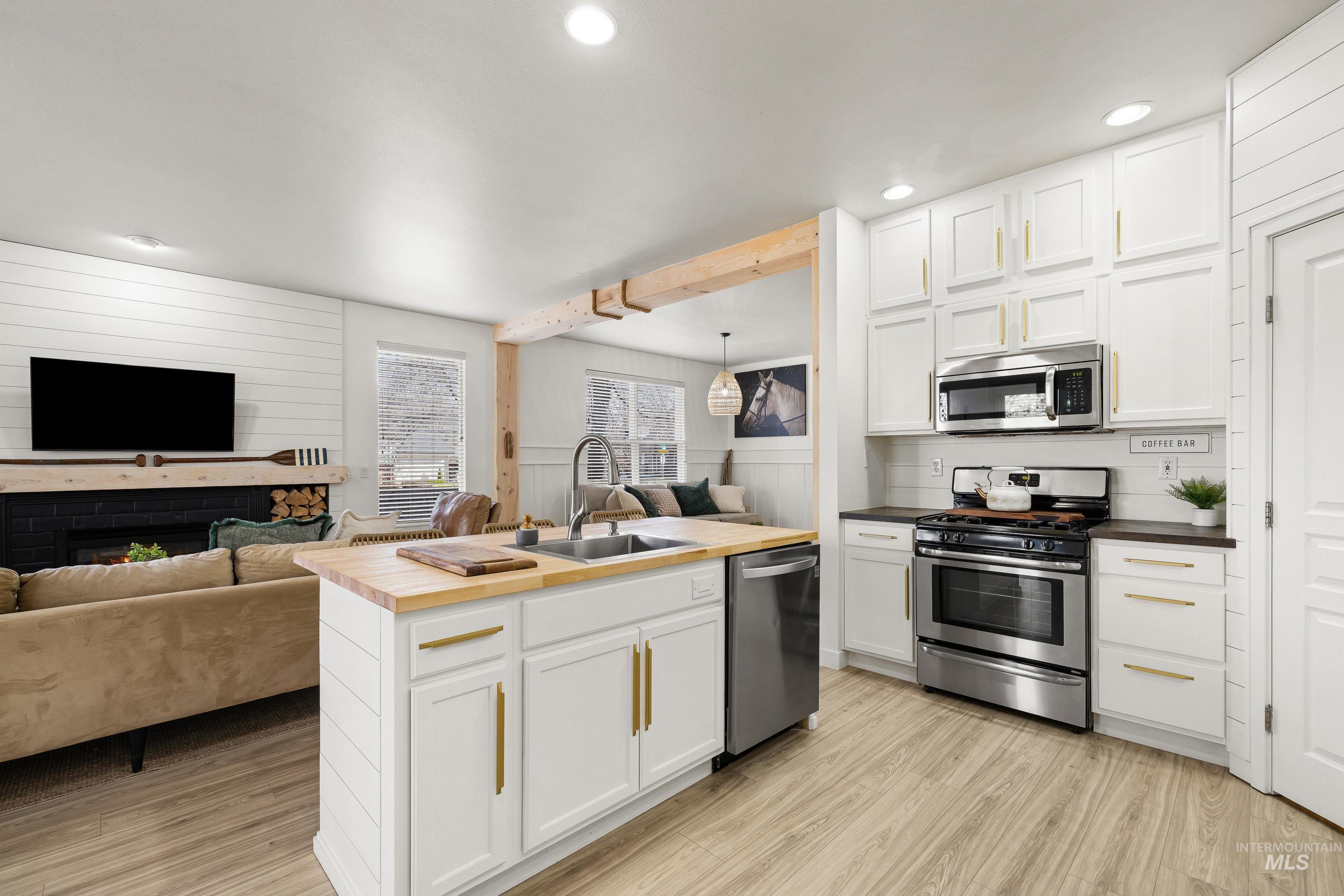 Kitchen with open floor plan, butcher block counters, stainless steel appliances, white cabinets, and wood walls
