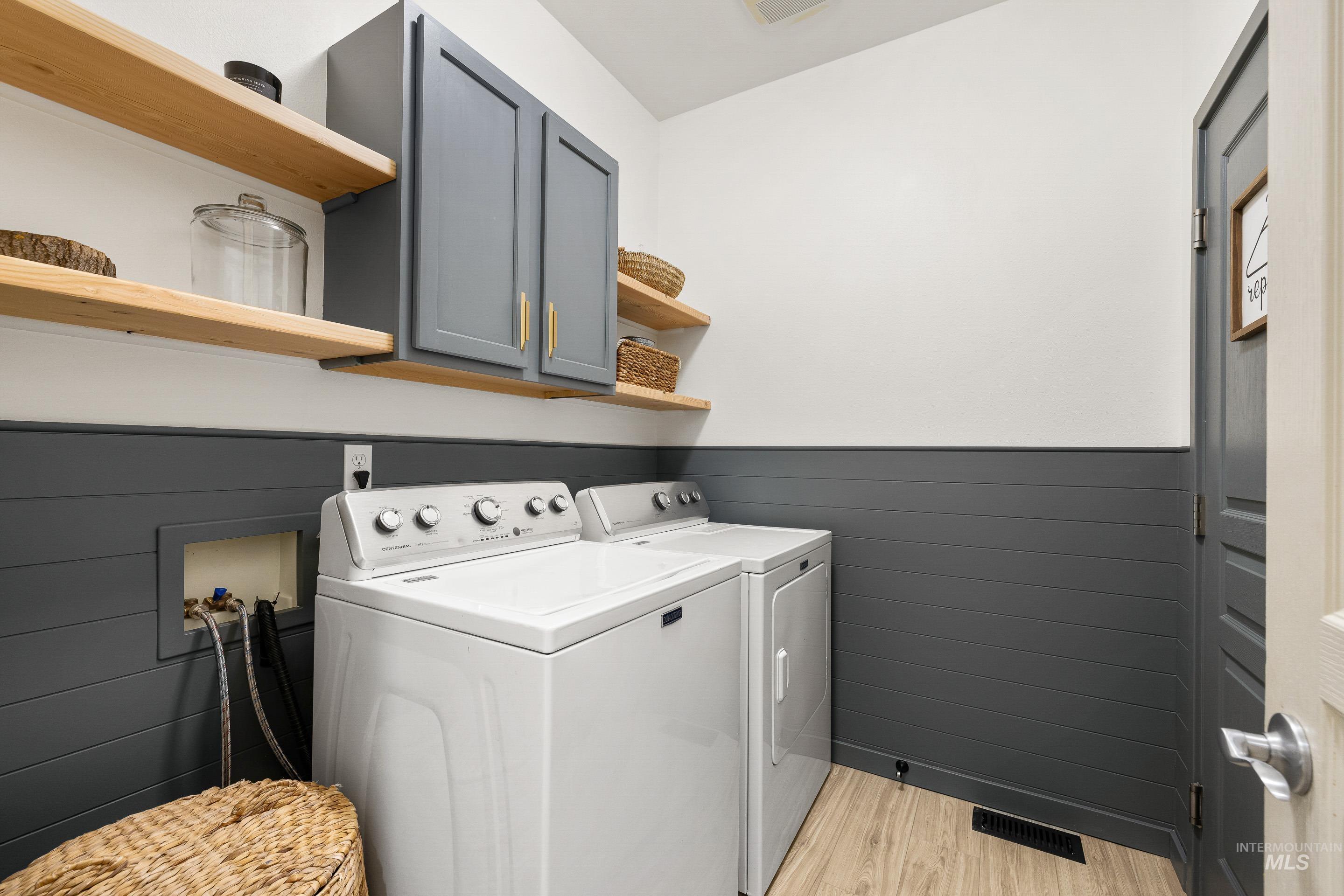 Laundry area featuring wainscoting, light wood finished floors, cabinet space, and independent washer and dryer