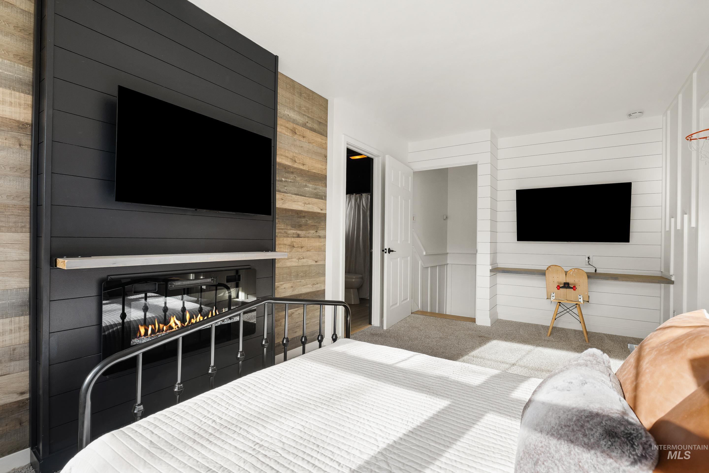 Bedroom with wooden walls, a large fireplace, carpet, and ensuite bathroom