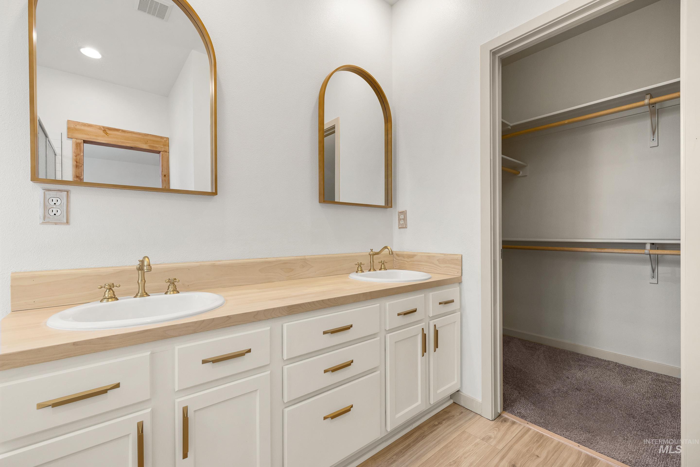 Bathroom featuring double vanity, light wood-style floors, and a walk in closet