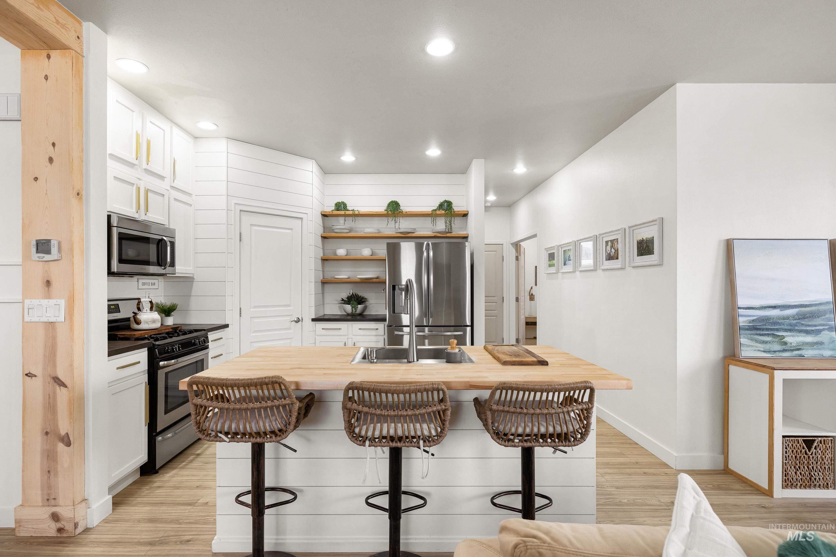 Kitchen featuring butcher block countertops, stainless steel appliances, light wood finished floors, open shelves, and white cabinets