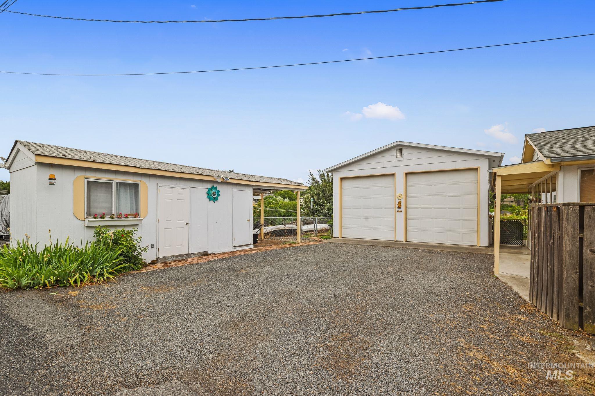 Gravel driveway with a two-car garage featuring dual garage doors and an adjacent storage shed with exterior window
