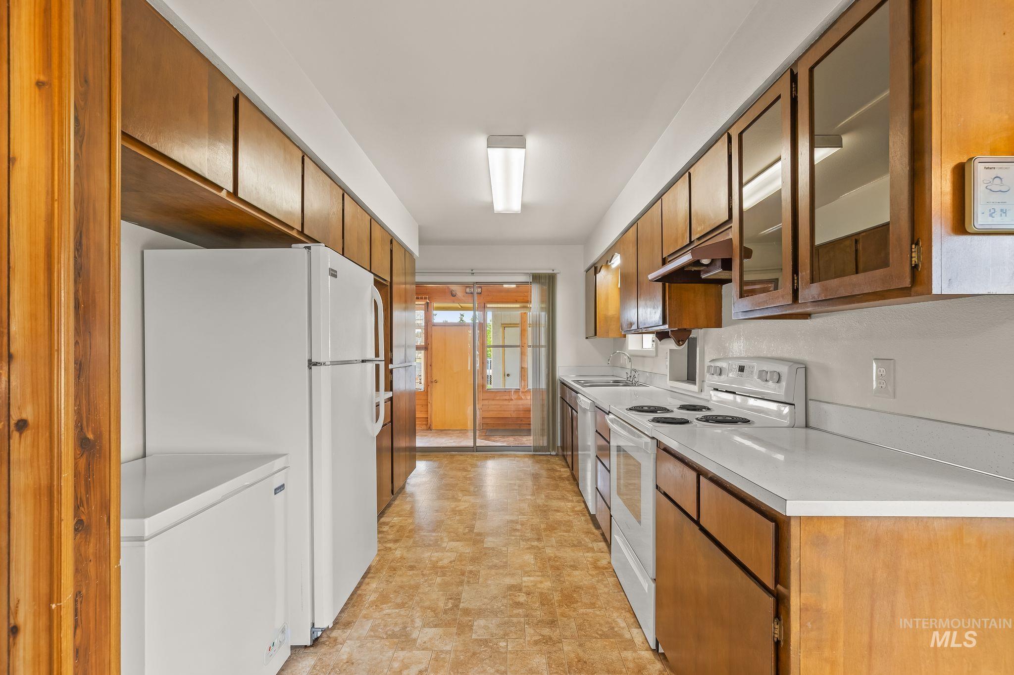 Galley kitchen featuring wood-finish cabinetry, white countertops, and integrated appliances