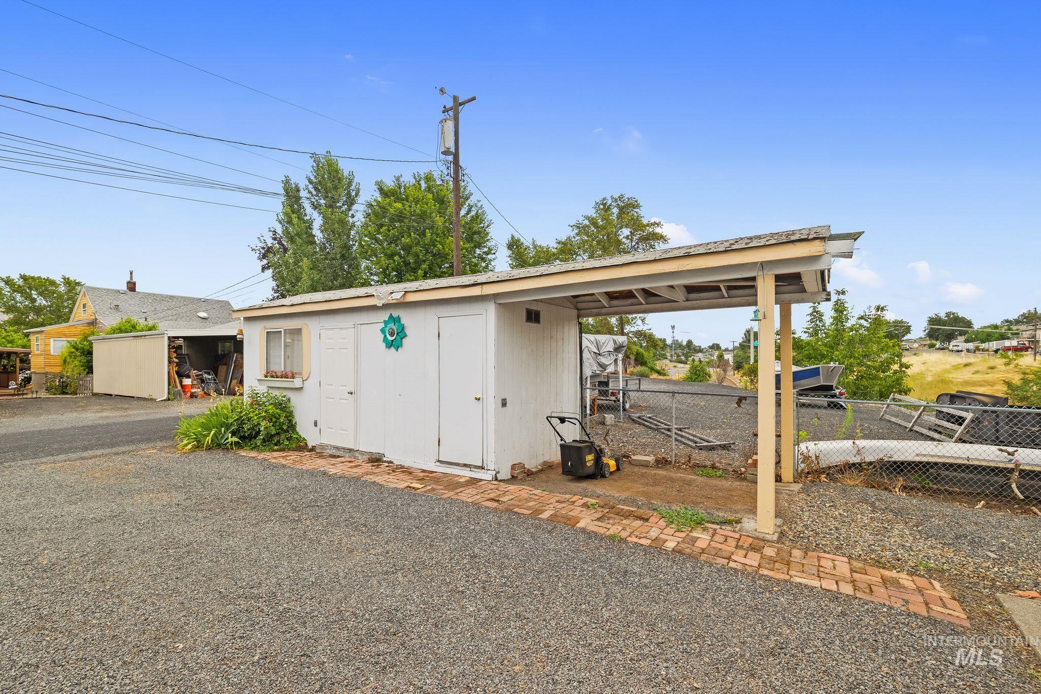 Detached outbuilding with an attached covered carport, featuring a window box, a brick pathway, and gravel surfacing