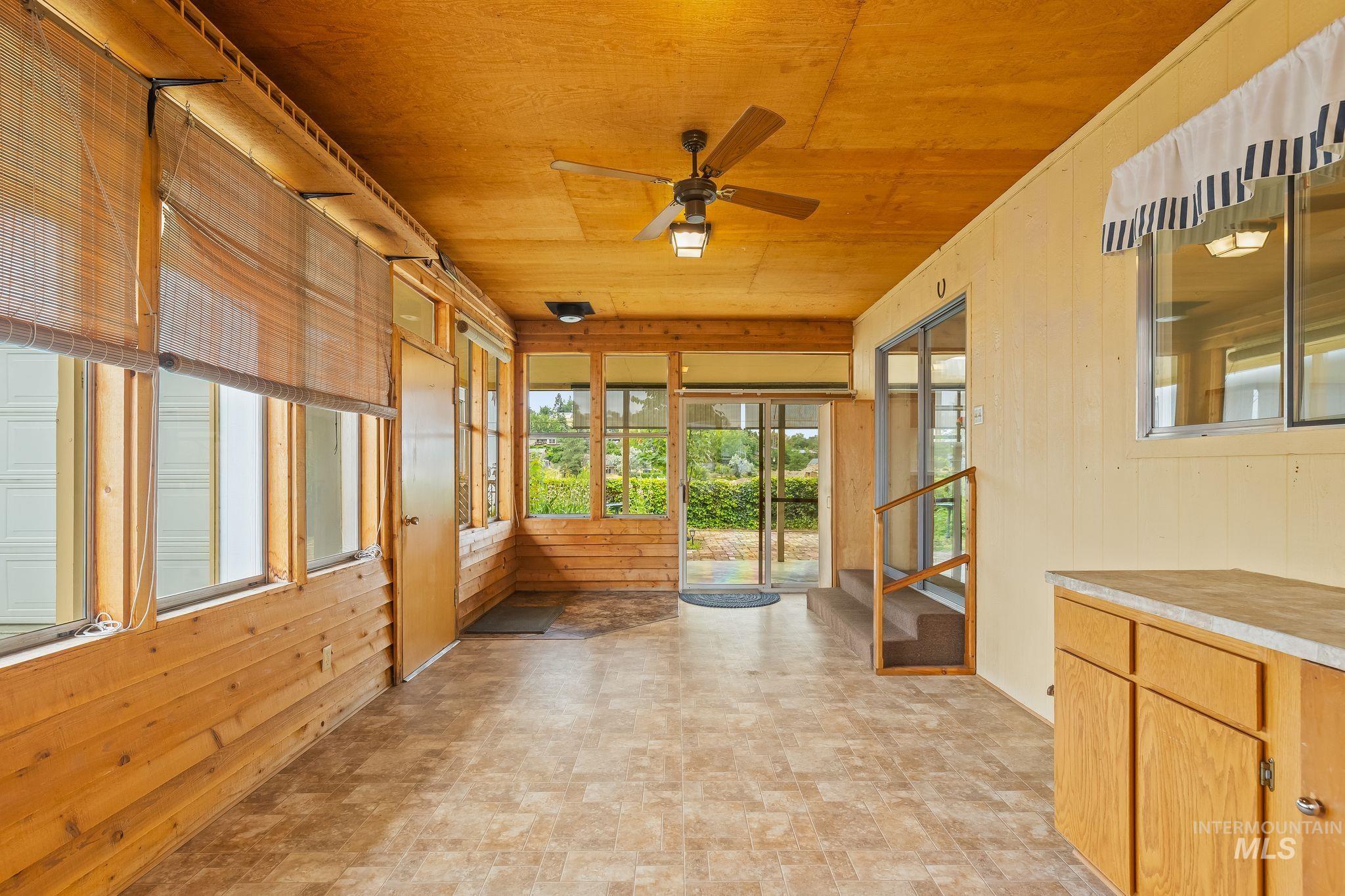 Enclosed sunroom featuring extensive window-lined walls, wood-paneled accents, and a ceiling fan