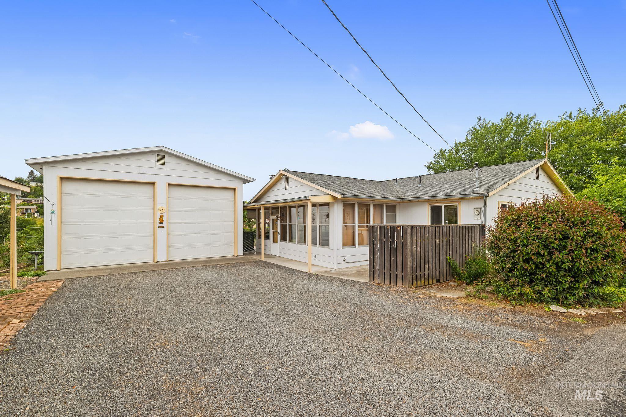 White-sided residence featuring a two-car garage, gravel driveway, and partial wood fencing
