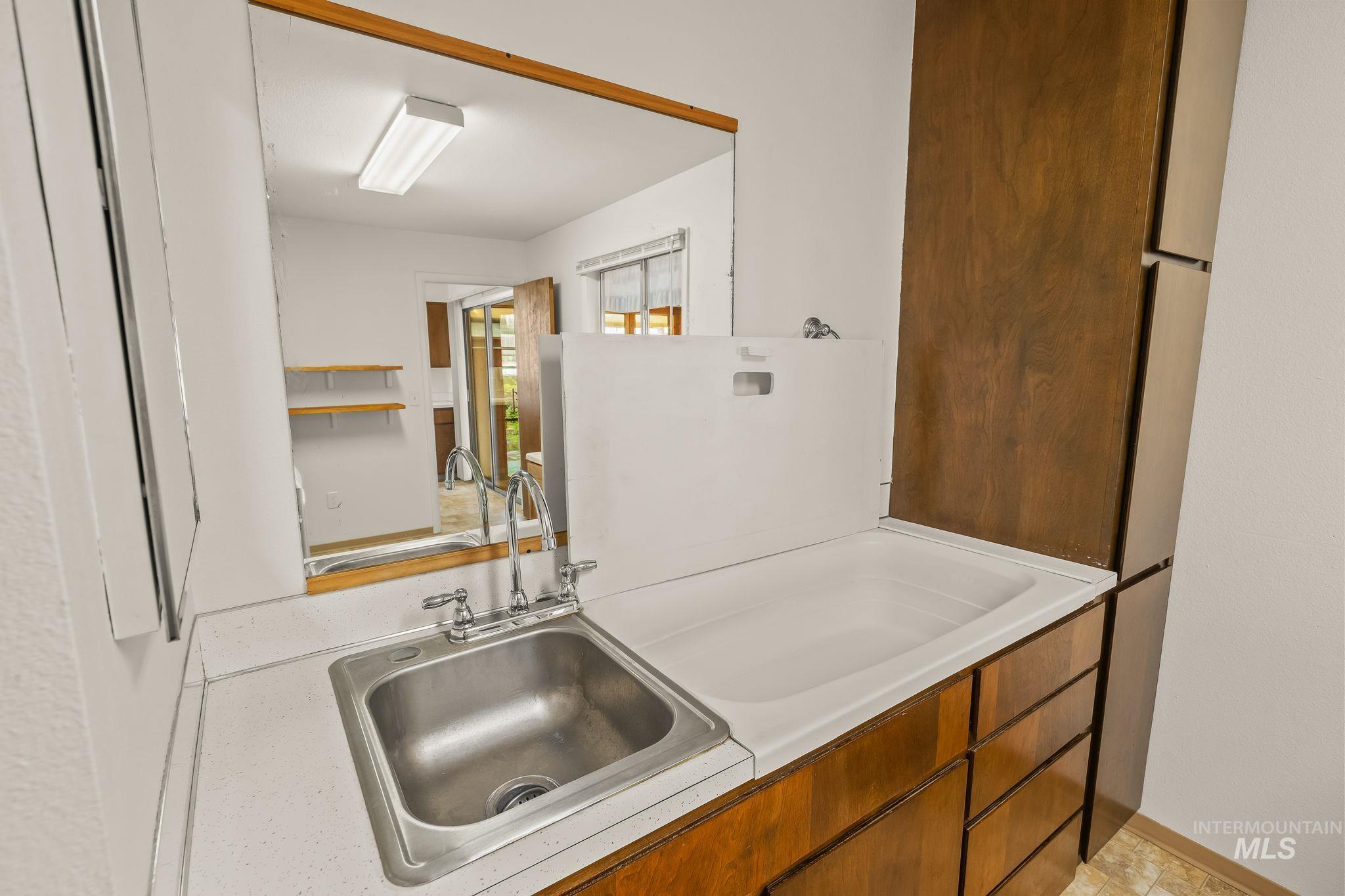 Utility room featuring a stainless steel sink, solid surface countertop, wood cabinetry, and a built-in laundry tub