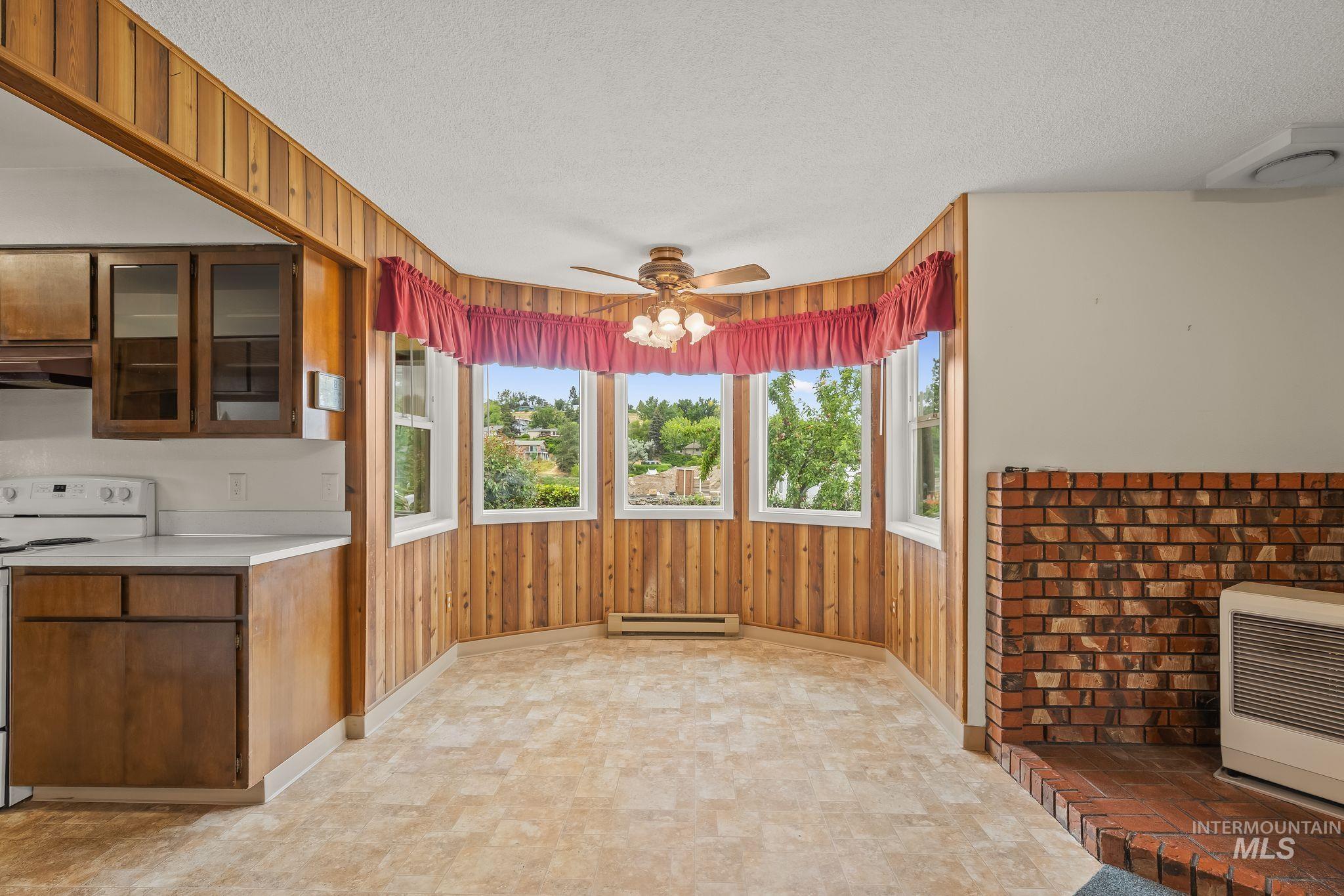Dining area featuring a bay window with natural light, wood paneling, and a ceiling fan