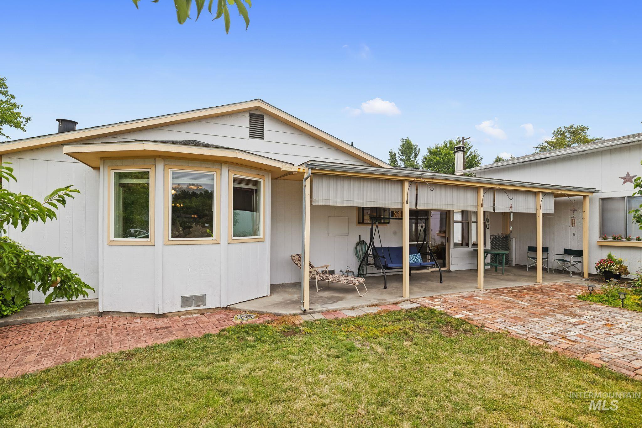 Rear exterior featuring a covered patio with a concrete slab and brick paver extension