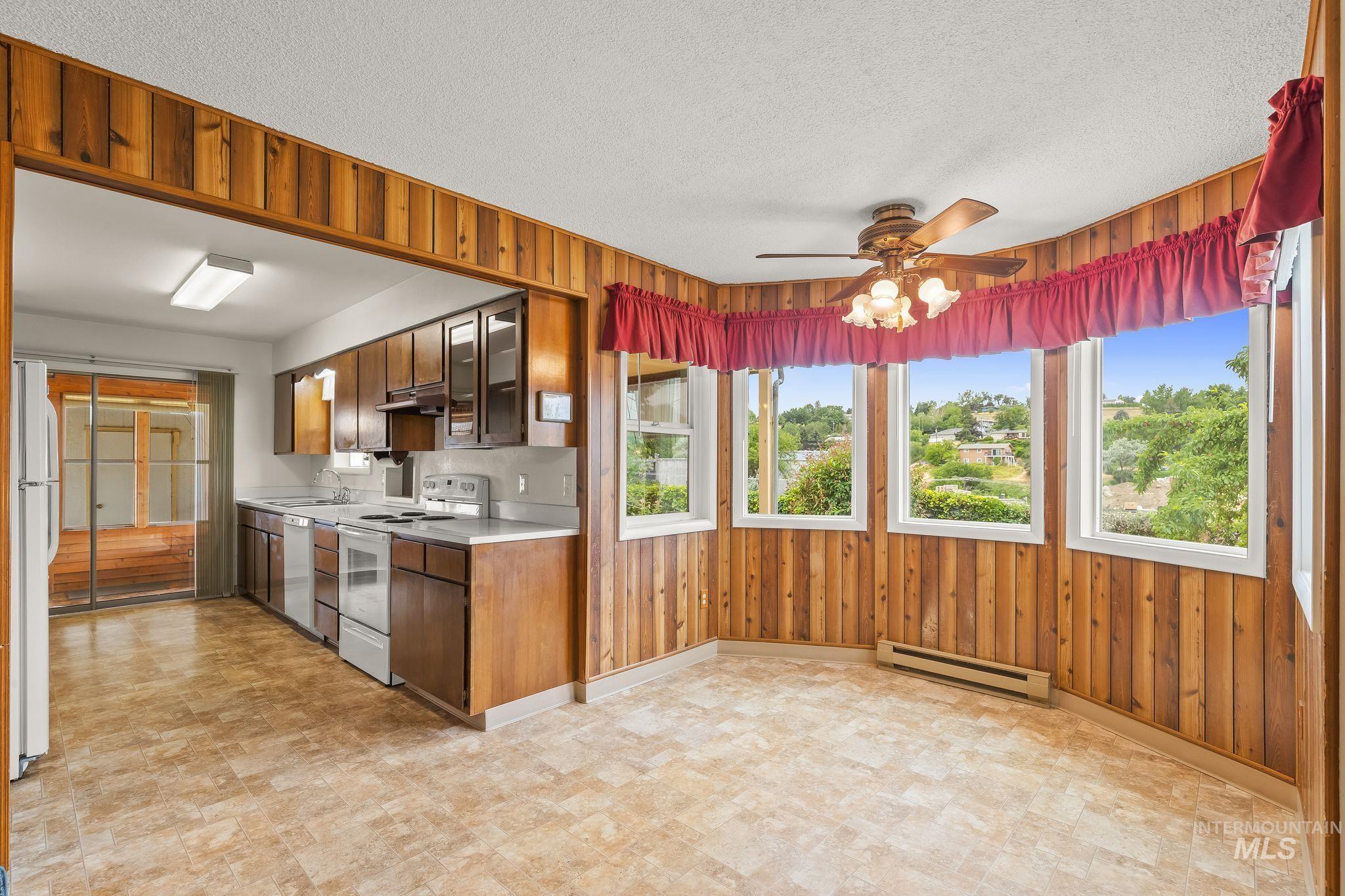 Kitchen and dining area featuring wood-paneled walls, multiple windows, a ceiling fan with integrated lighting, and resilient flooring