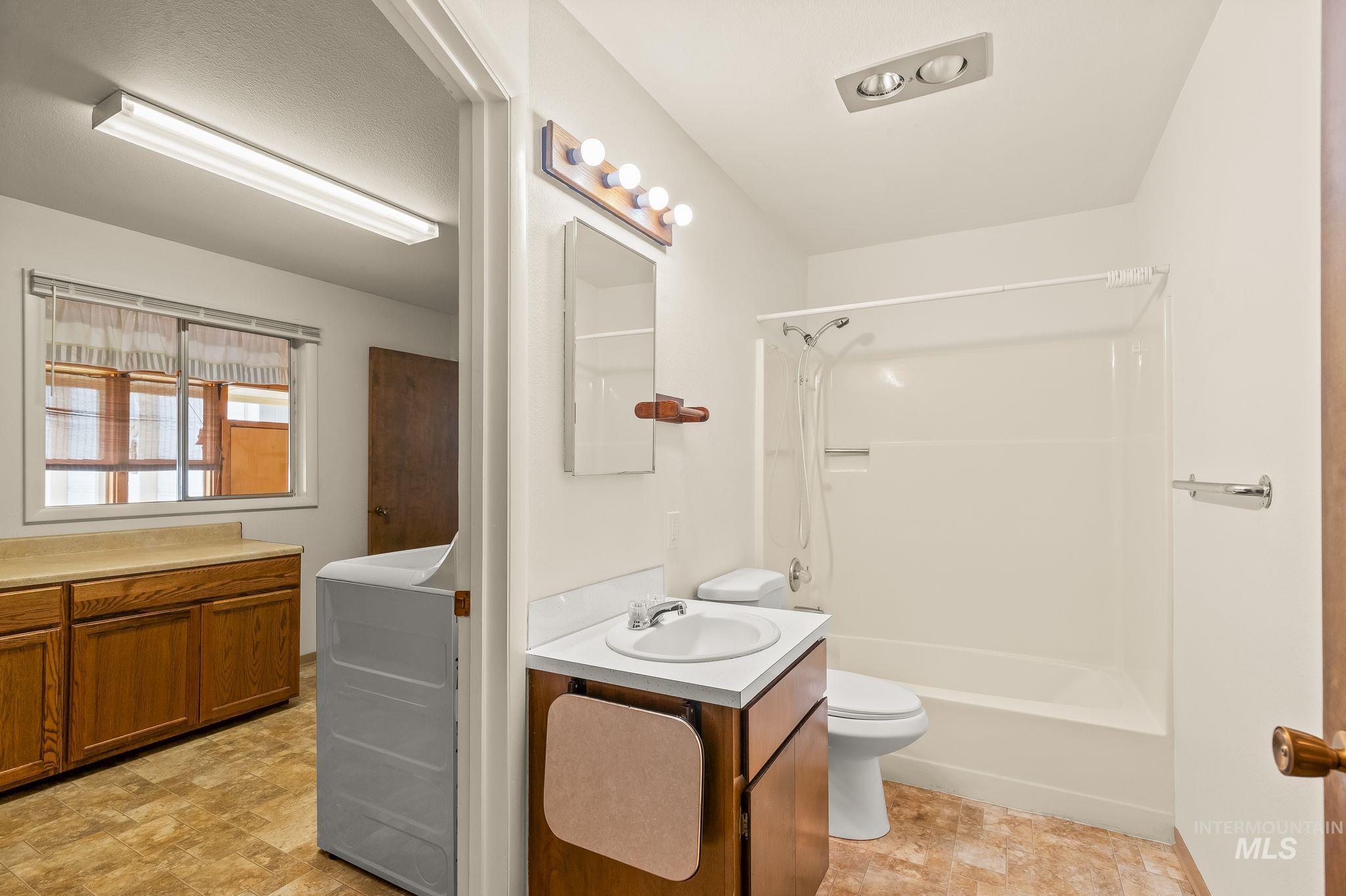 Bathroom featuring a white vanity with integrated sink, a commode, and a shower-tub combination with white surround