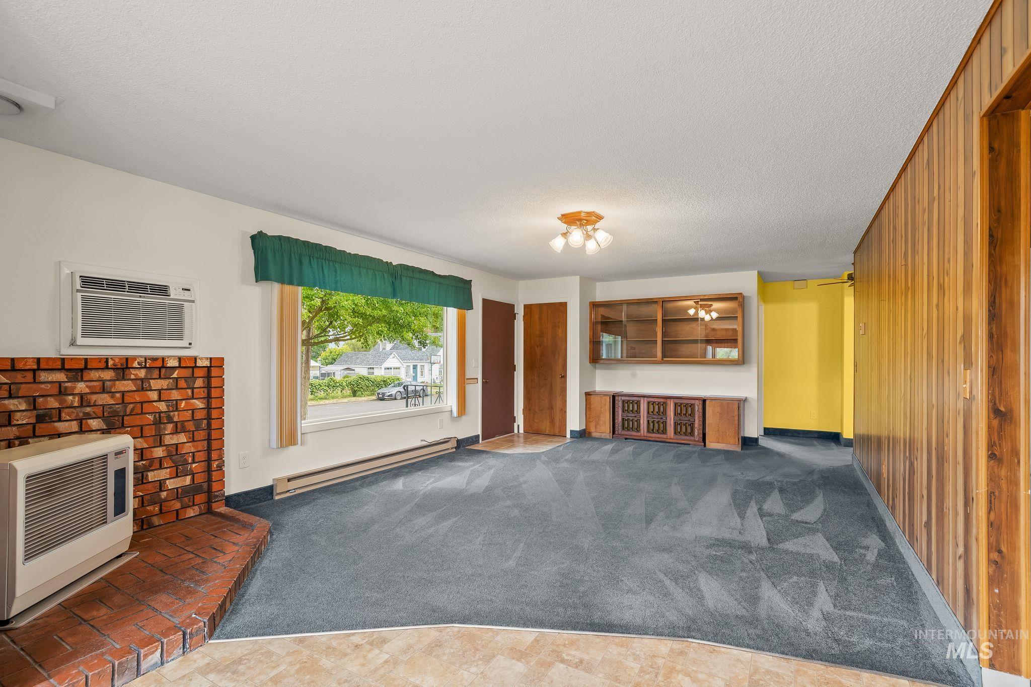 Living area featuring a brick fireplace, built-in display cabinetry, wood paneling, and a large front-facing window