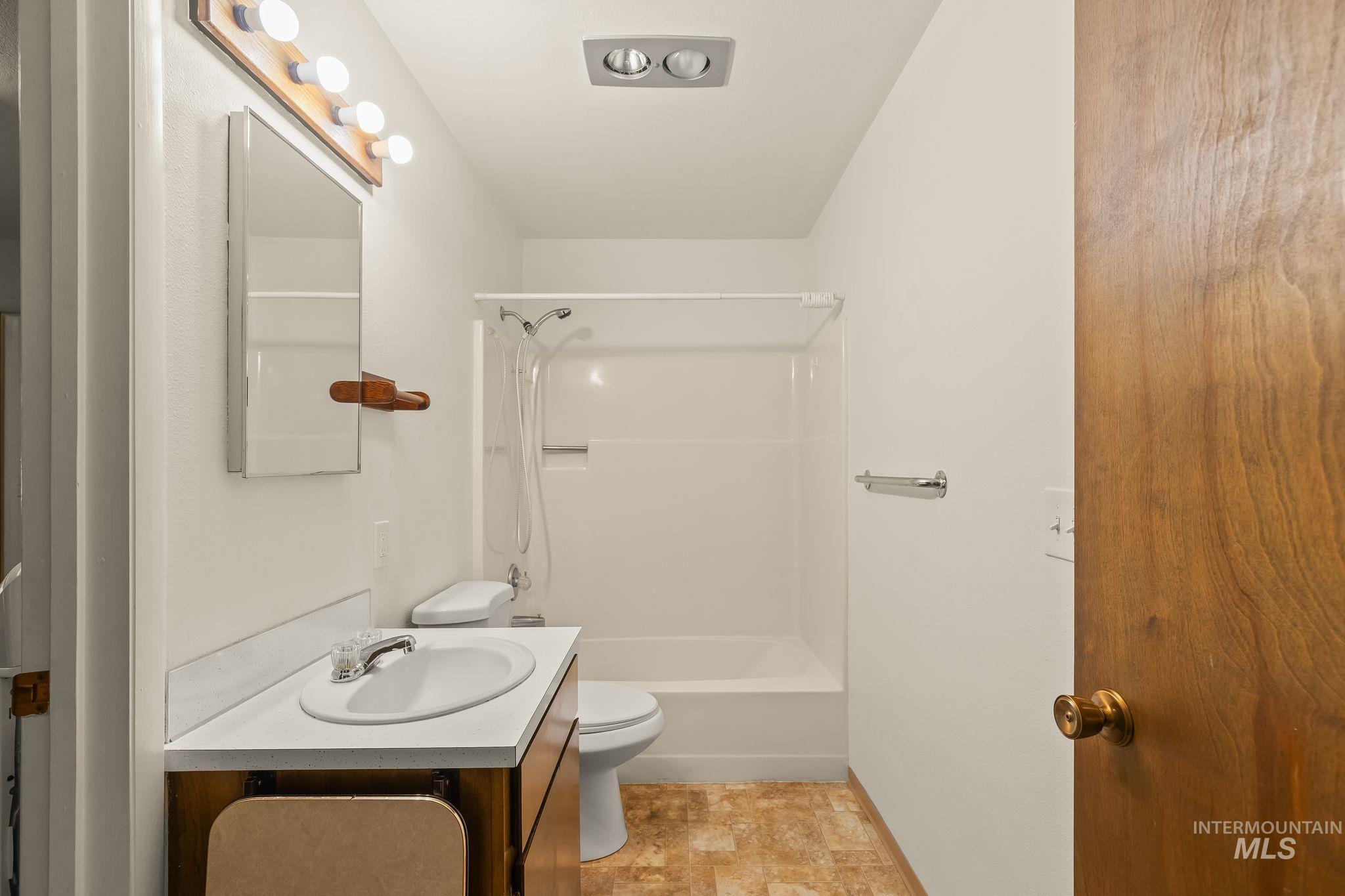 Full bathroom featuring a single vanity with an integrated sink, a combination tub and shower unit, and wood-finish flooring
