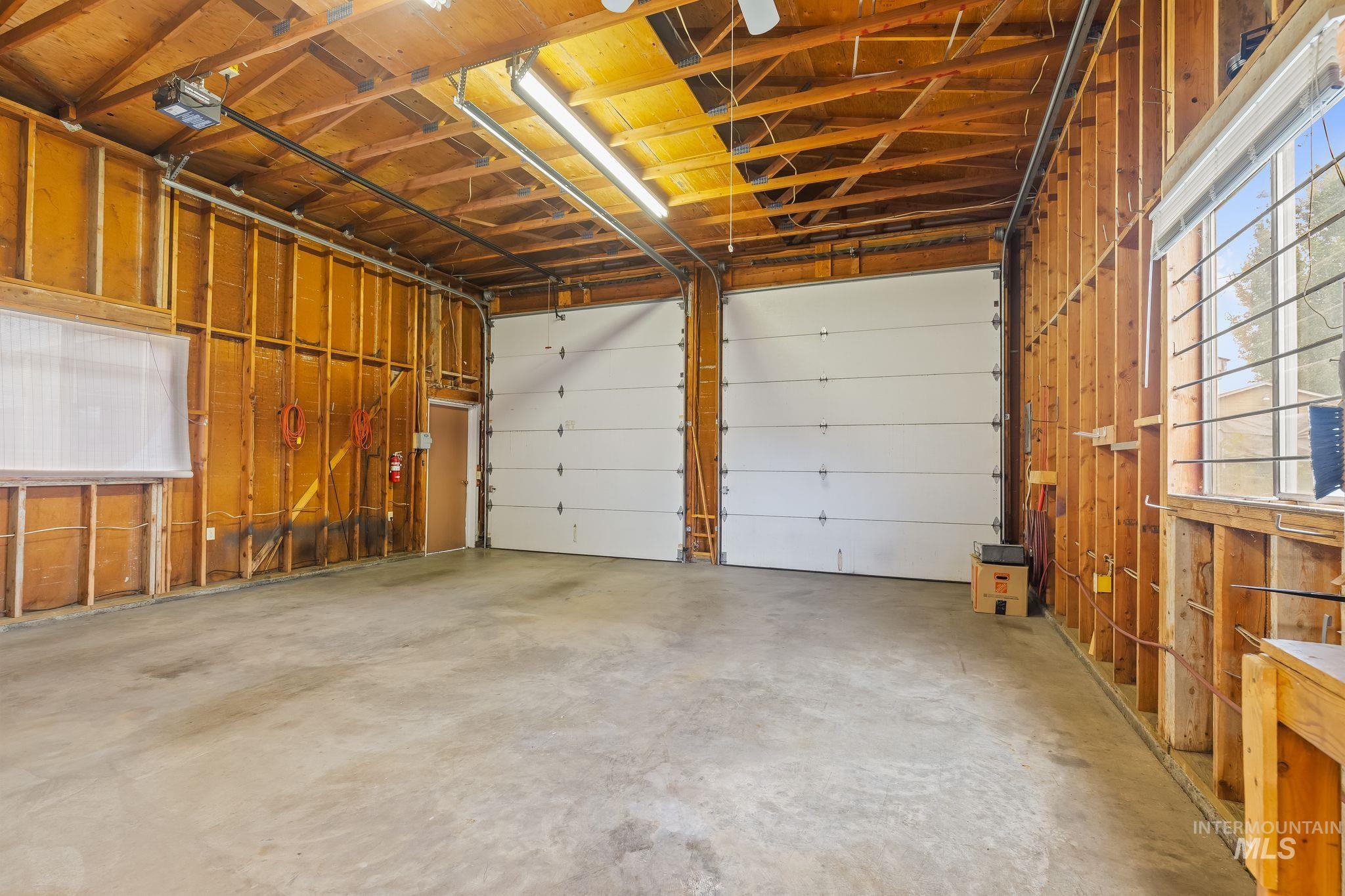 Spacious garage featuring two overhead doors, exposed wood framing, concrete flooring, and ample natural light from multiple windows