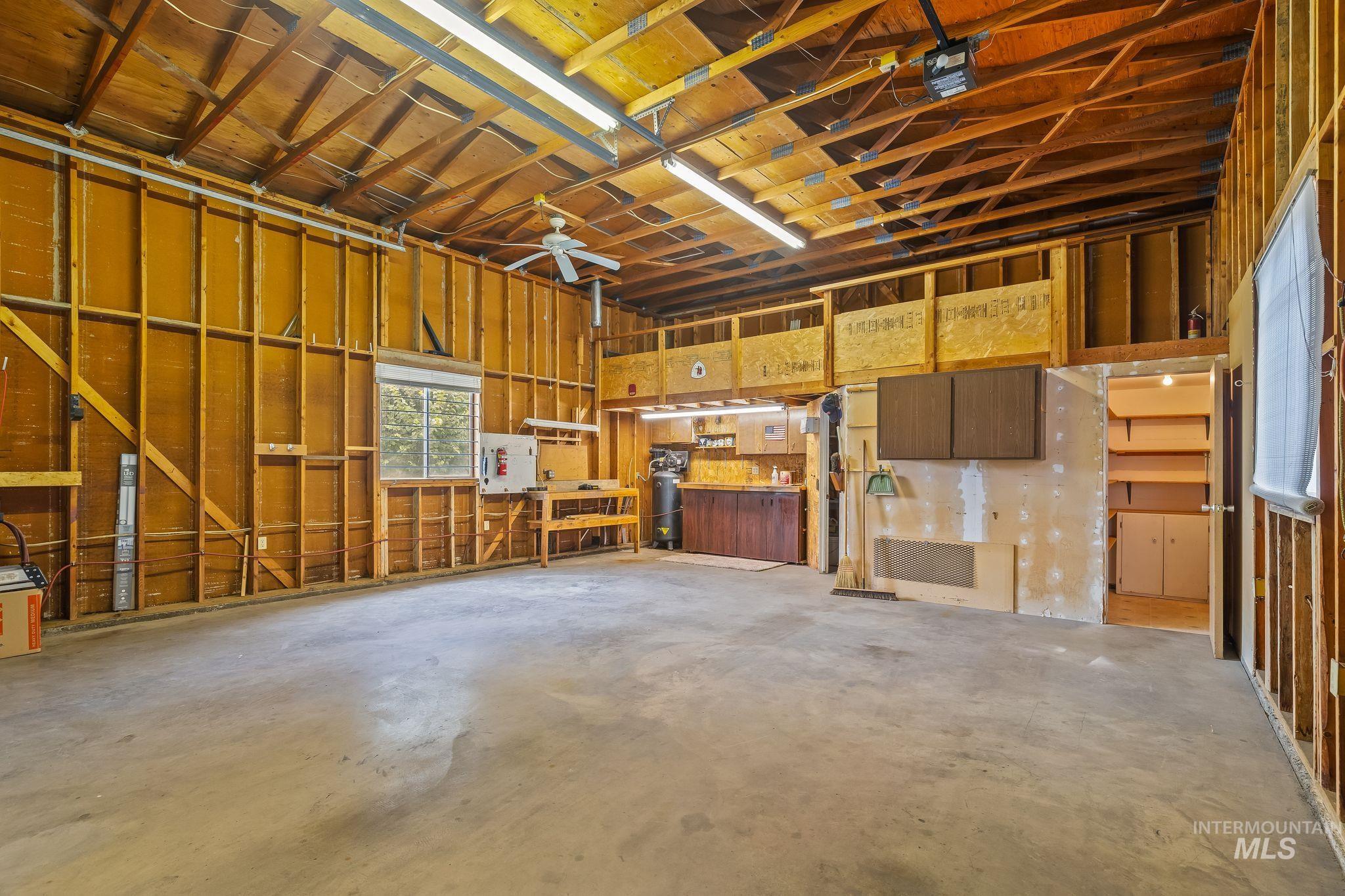 Spacious garage interior featuring an exposed wood-beam ceiling, concrete flooring, and a ceiling fan