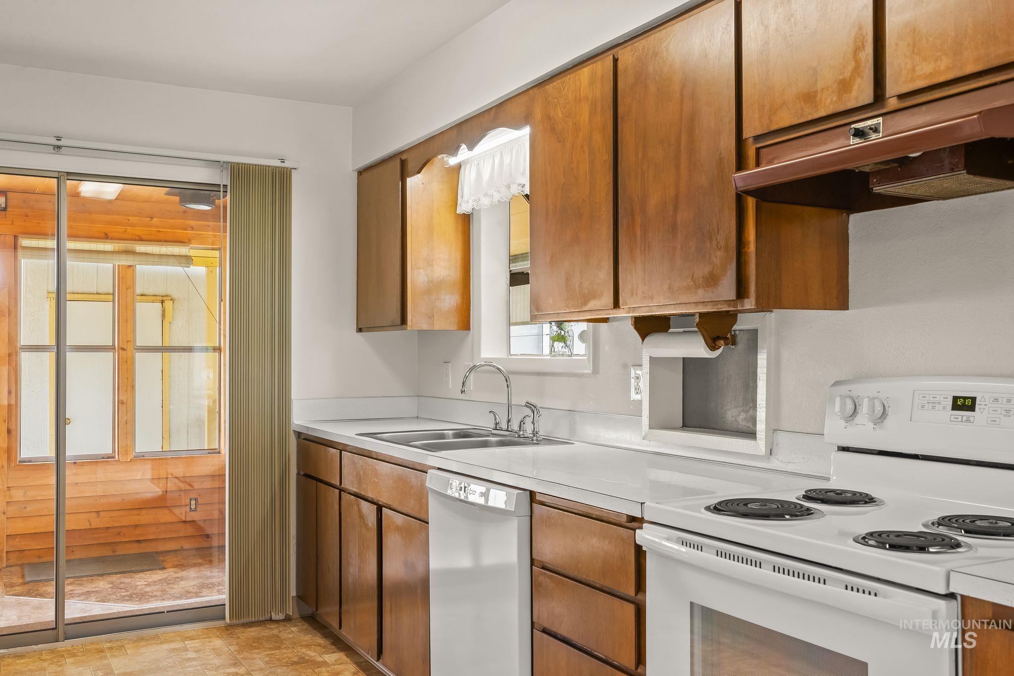 Kitchen featuring wood-finish cabinetry, white countertops, a double basin stainless steel sink, and a white electric range