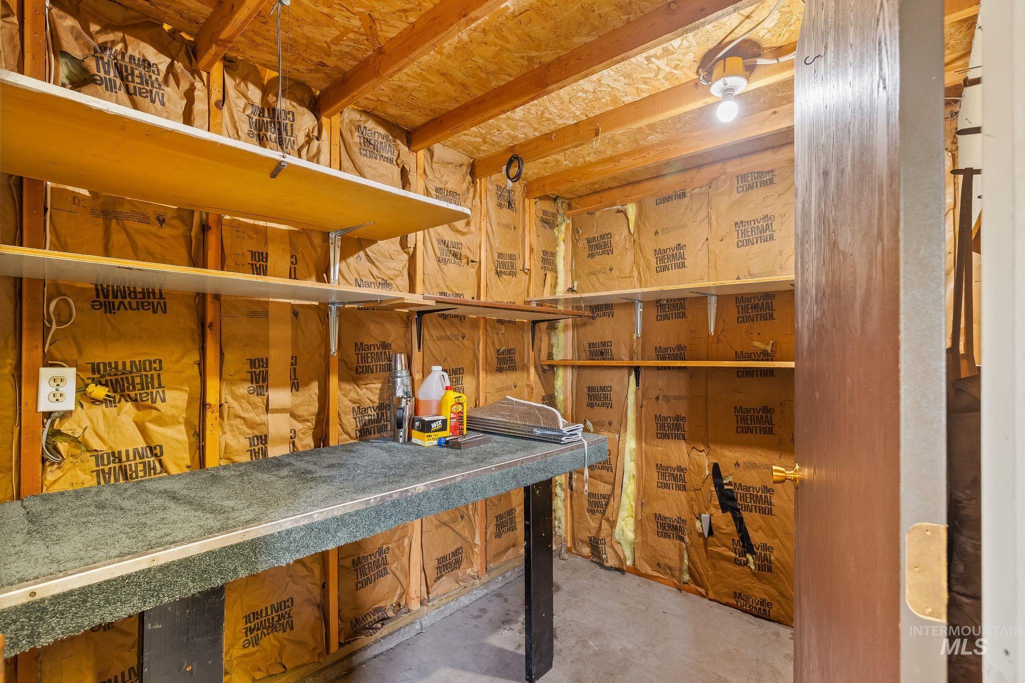 Utility room featuring open wood shelving, a built-in workbench, exposed insulation, a single light fixture, and a solid-core door