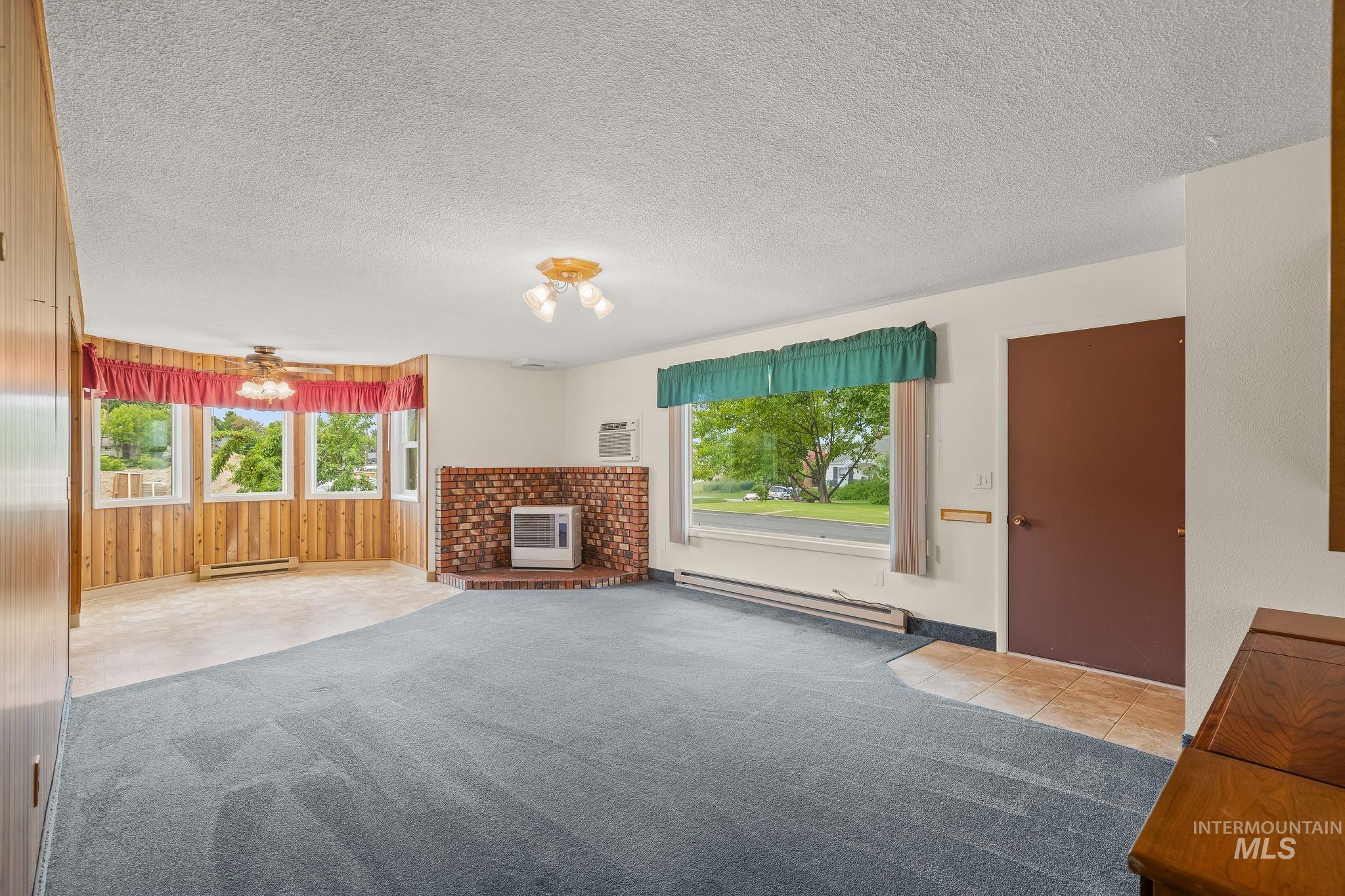 Spacious living area featuring a brick fireplace, bay window, wood-finish wall paneling, and a ceiling fan
